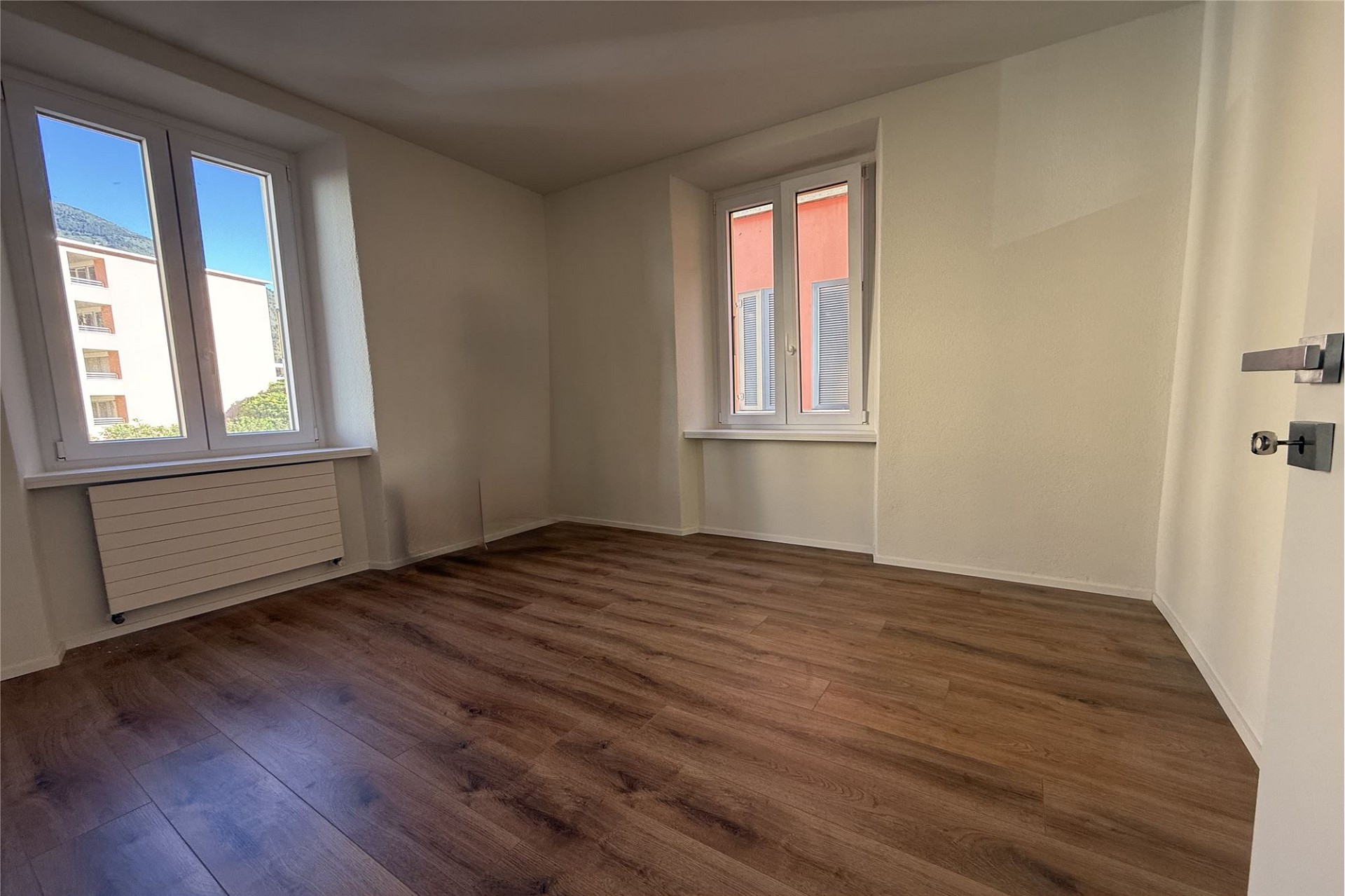 Heller leerer Raum mit zwei Fenstern und Holzboden