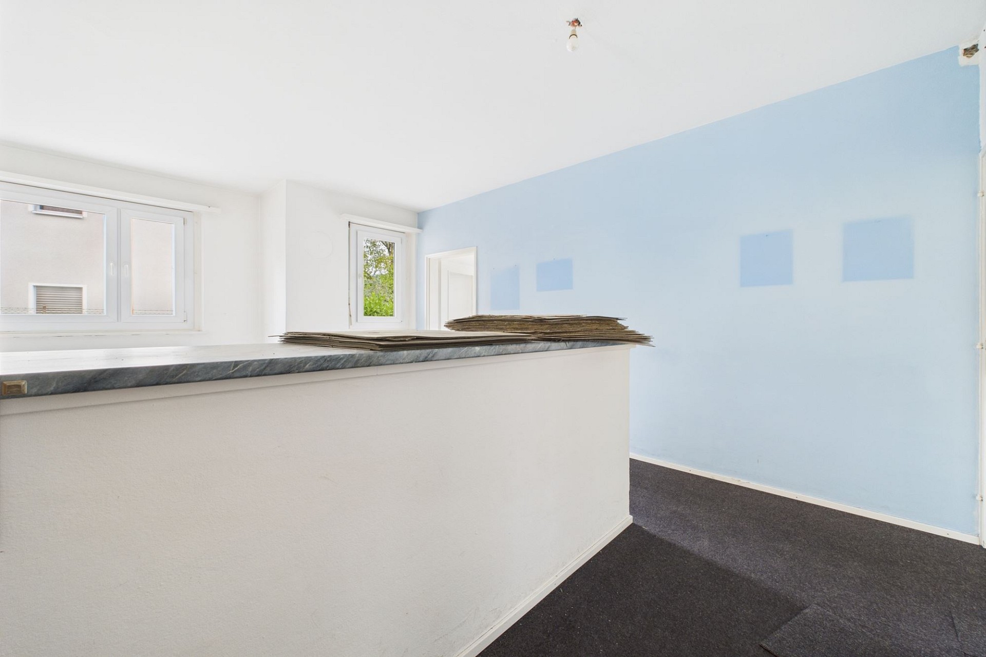 Kleiner heller Raum mit Fensterfront und blauer Akzentwand