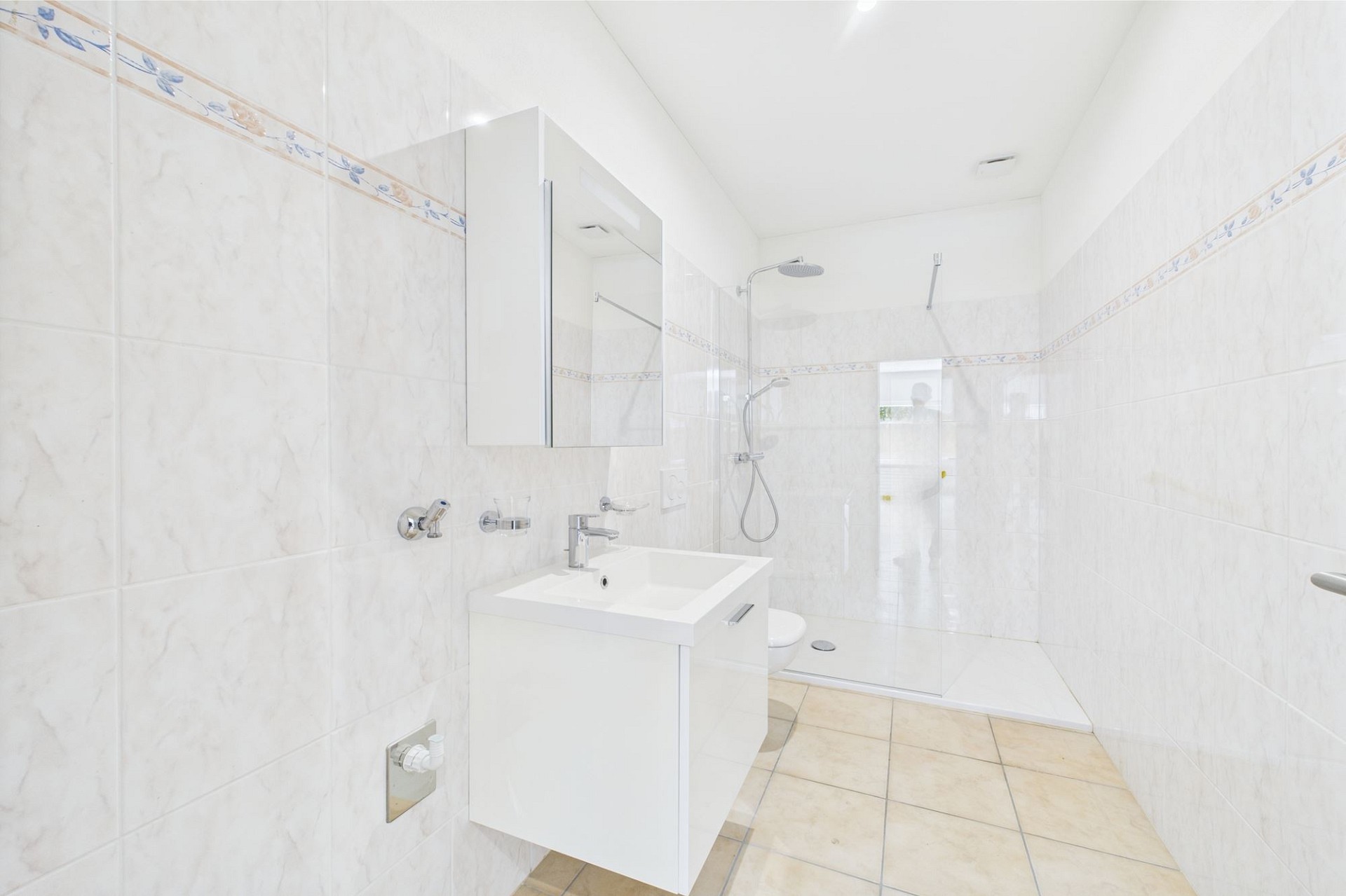 Helles, gefliestes Badezimmer mit Dusche und Waschtisch