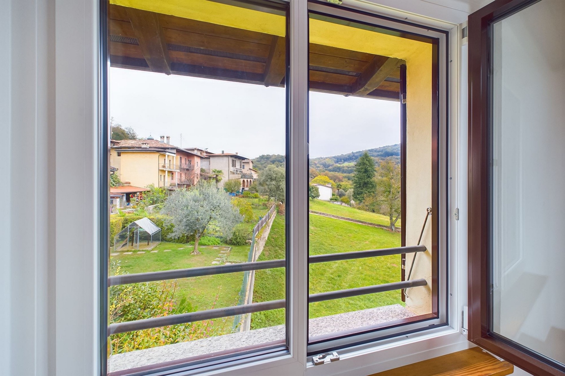 Blick aus einem geöffneten Fenster auf Garten und Hügellandschaft