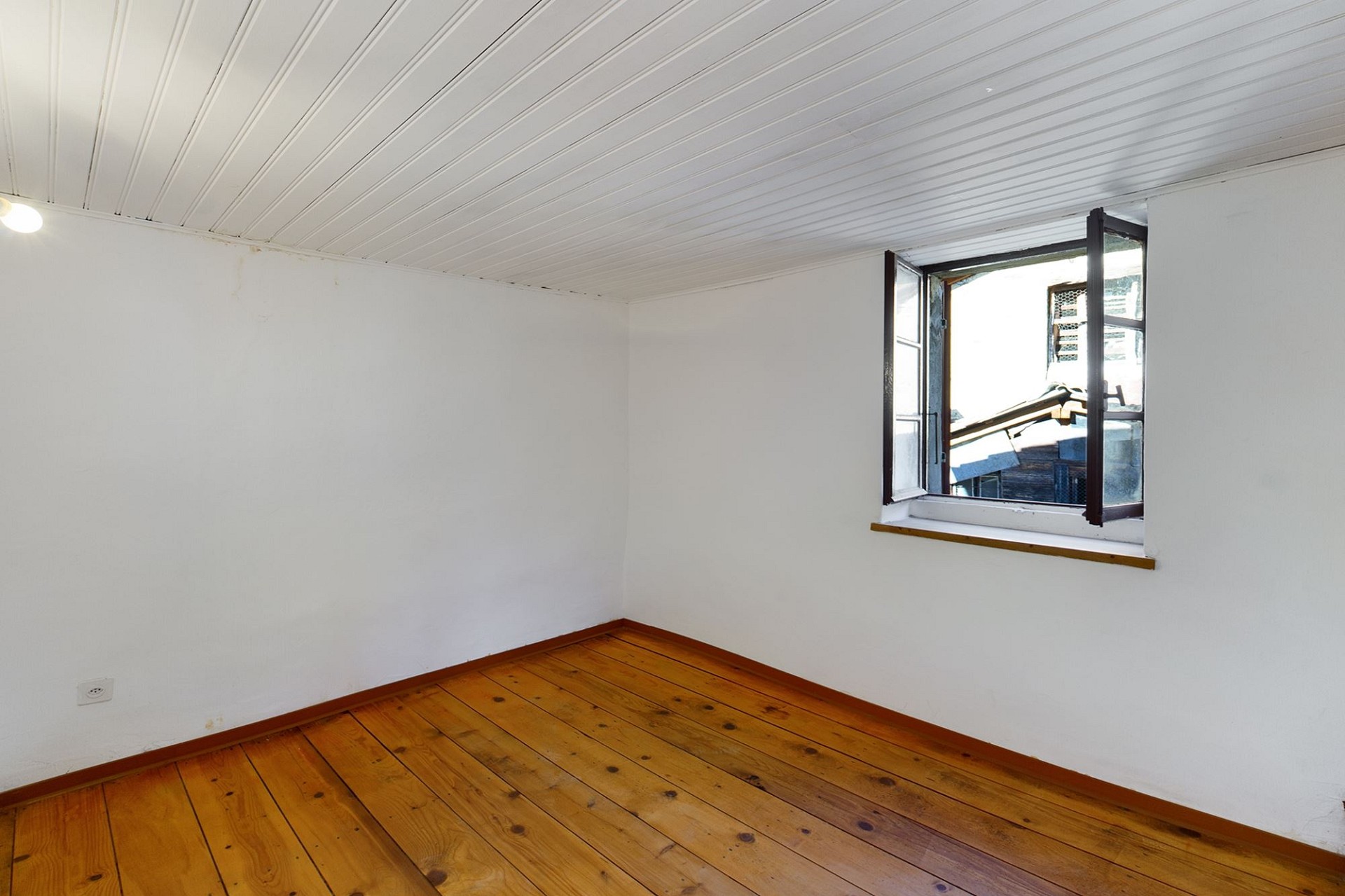 Ein leerer, heller Raum mit Holzfußboden und offenem Fenster