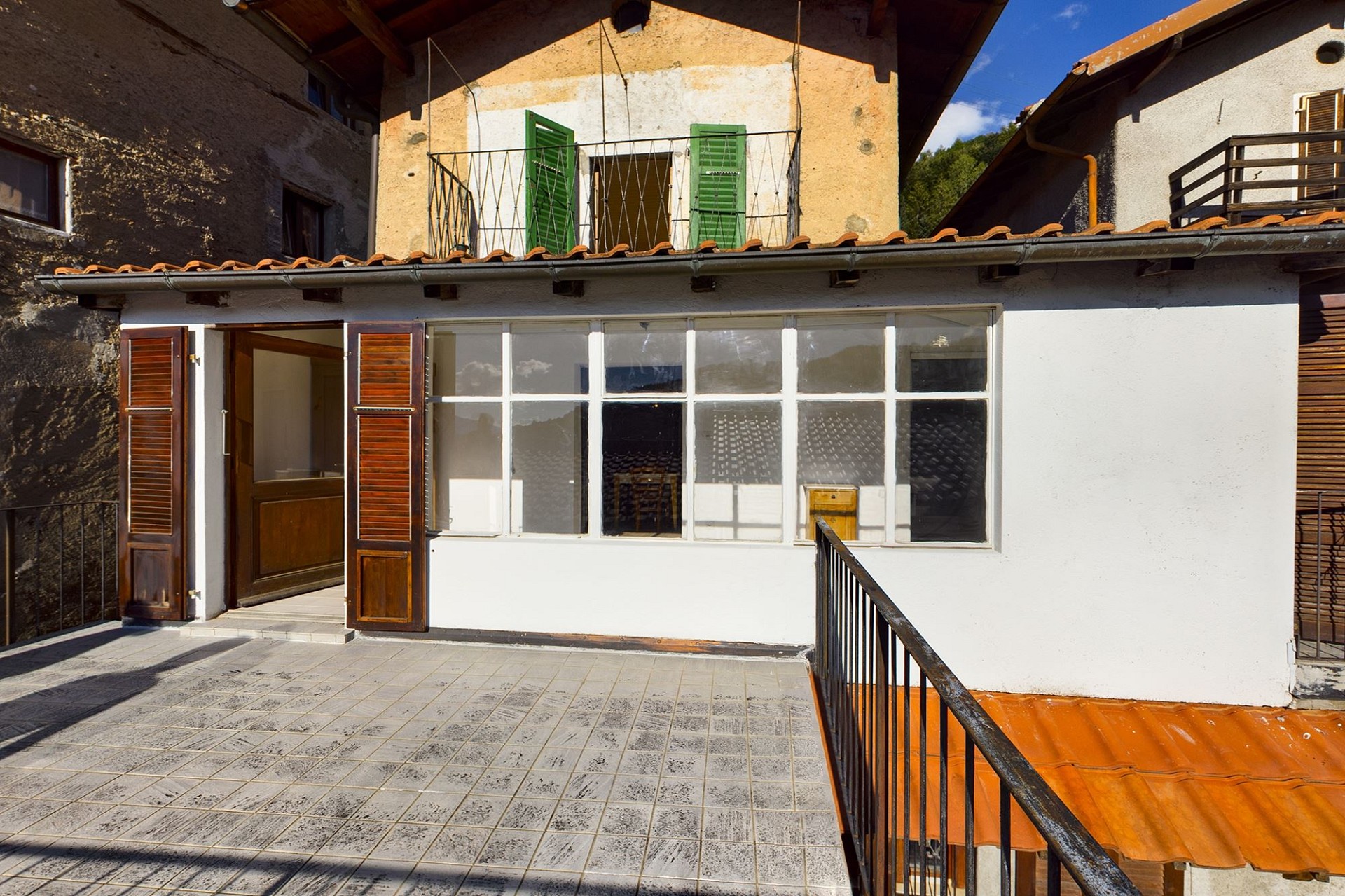Terrasse vor einem älteren Wohnhaus mit Balkon und grünen Fensterläden