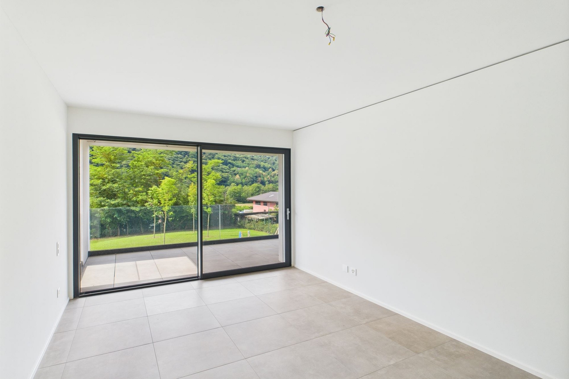 Leerer moderner Raum mit großer Schiebetür und Gartenblick