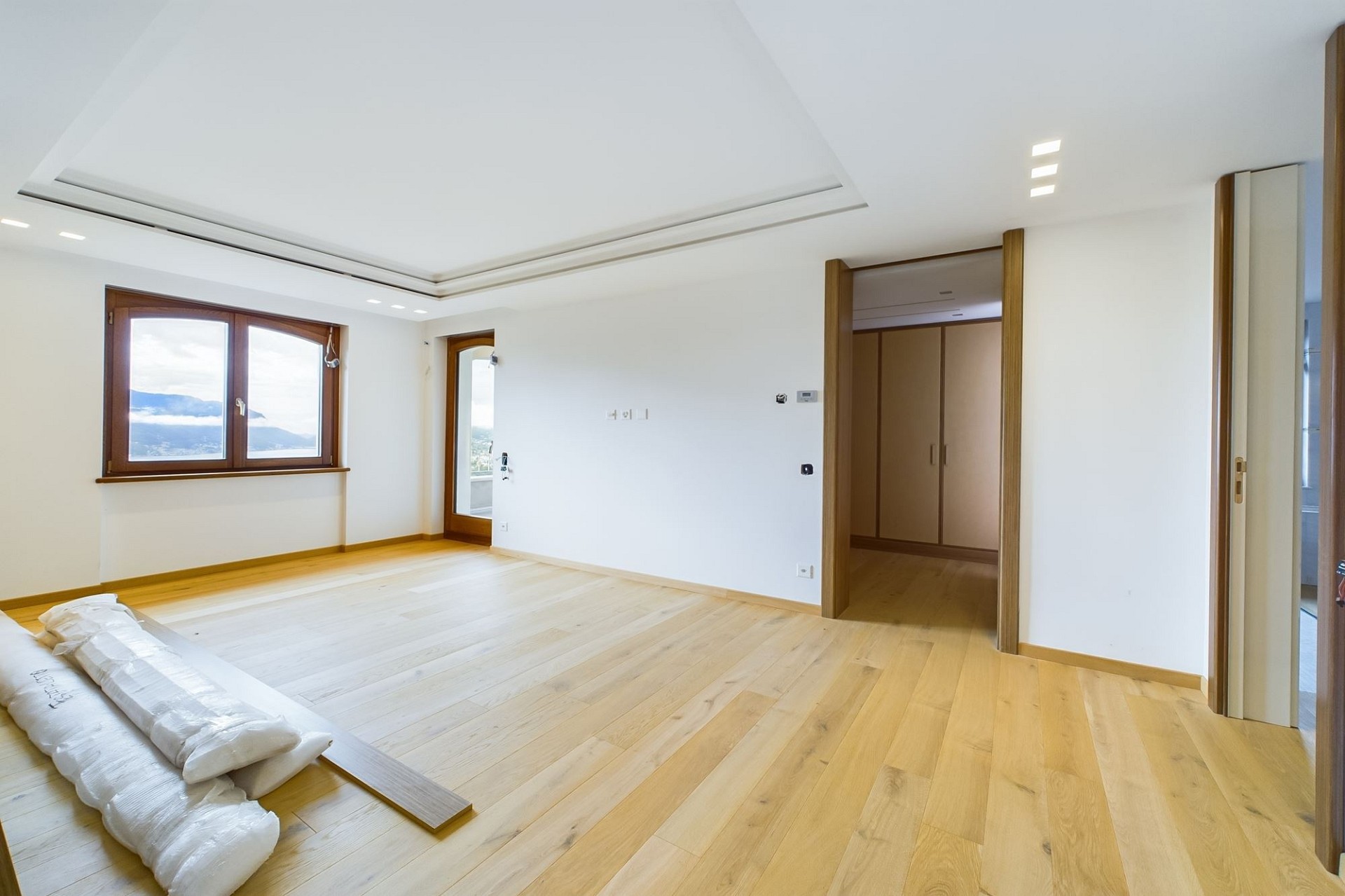 Helles, leeres Schlafzimmer mit Holzparkett und Blick ins Grüne