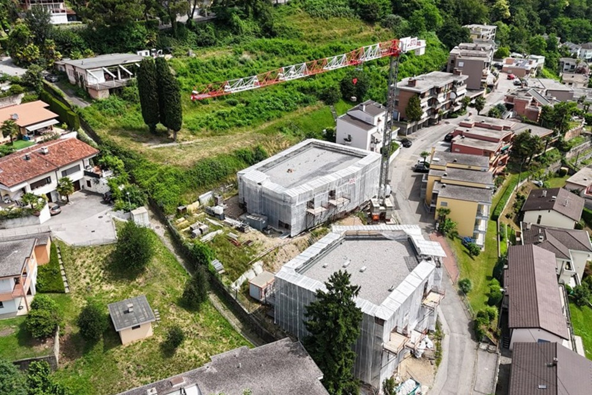 Luftaufnahme eines Wohngebiets mit zwei Gebäuden im Bau und grüner Hanglage