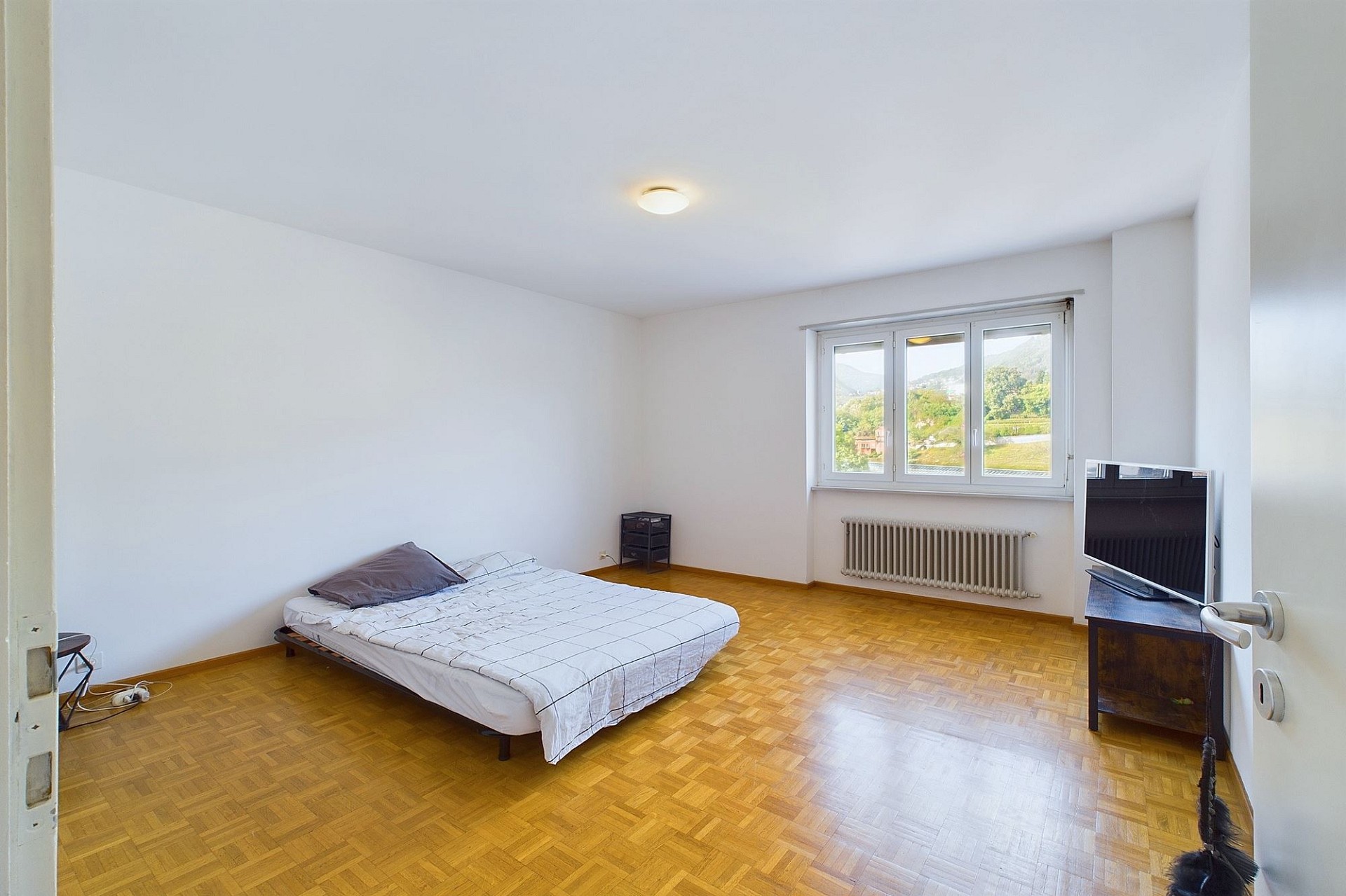 Helles, schlicht möbliertes Schlafzimmer mit Parkettboden und Bergblick