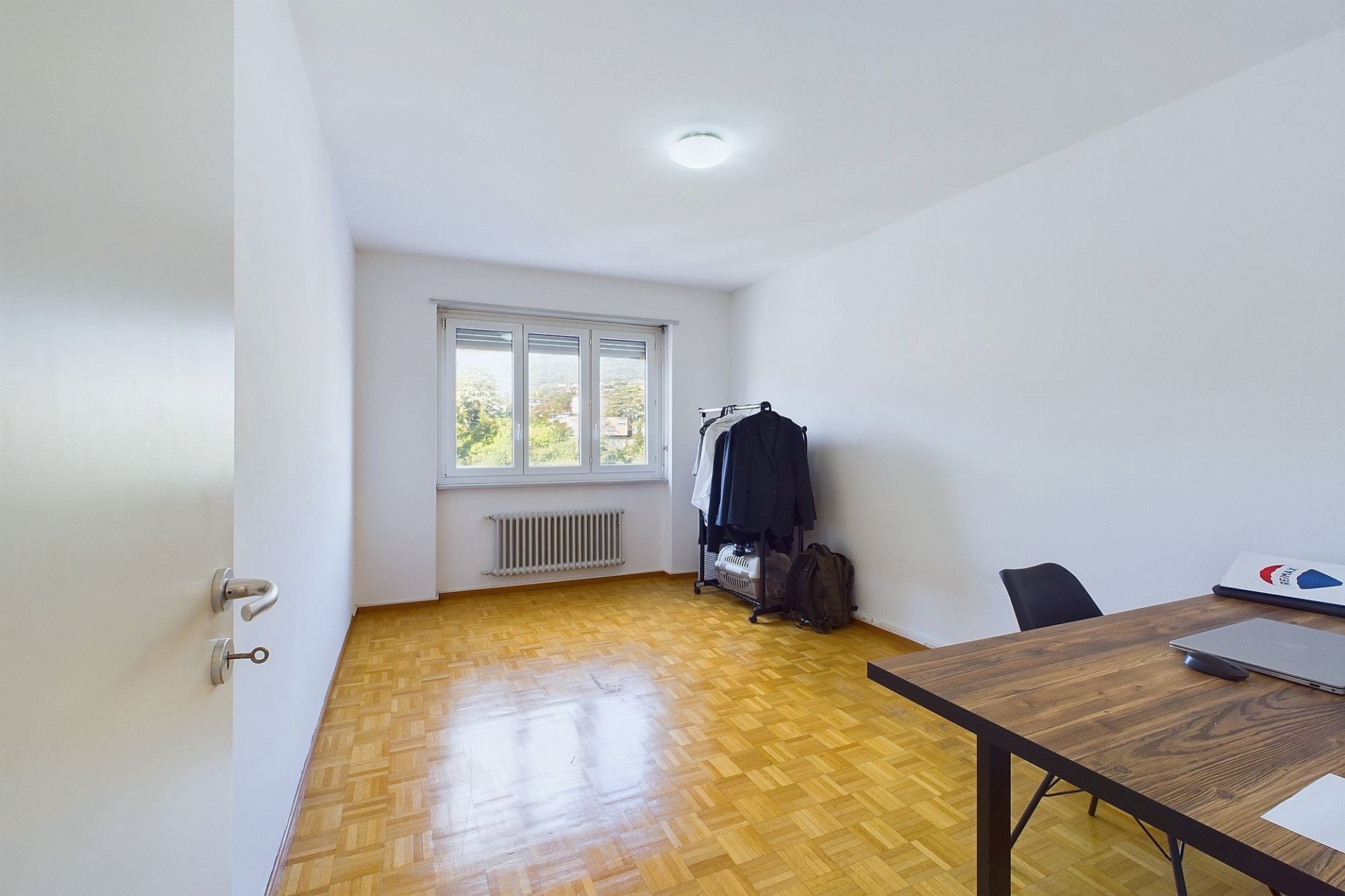 Helles, leer geräumtes Zimmer mit Parkettboden und Fenster