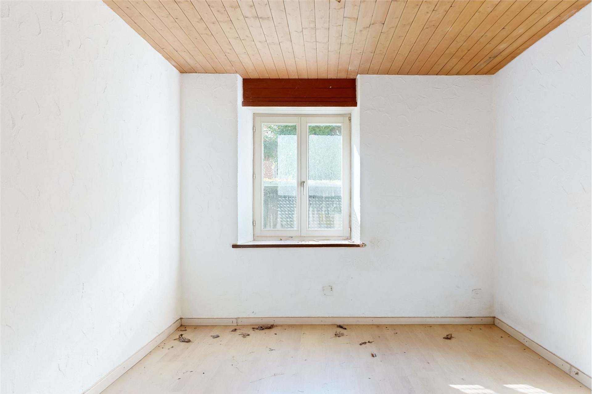 Heller leerer Raum mit Holzdecke und kleinem Fenster