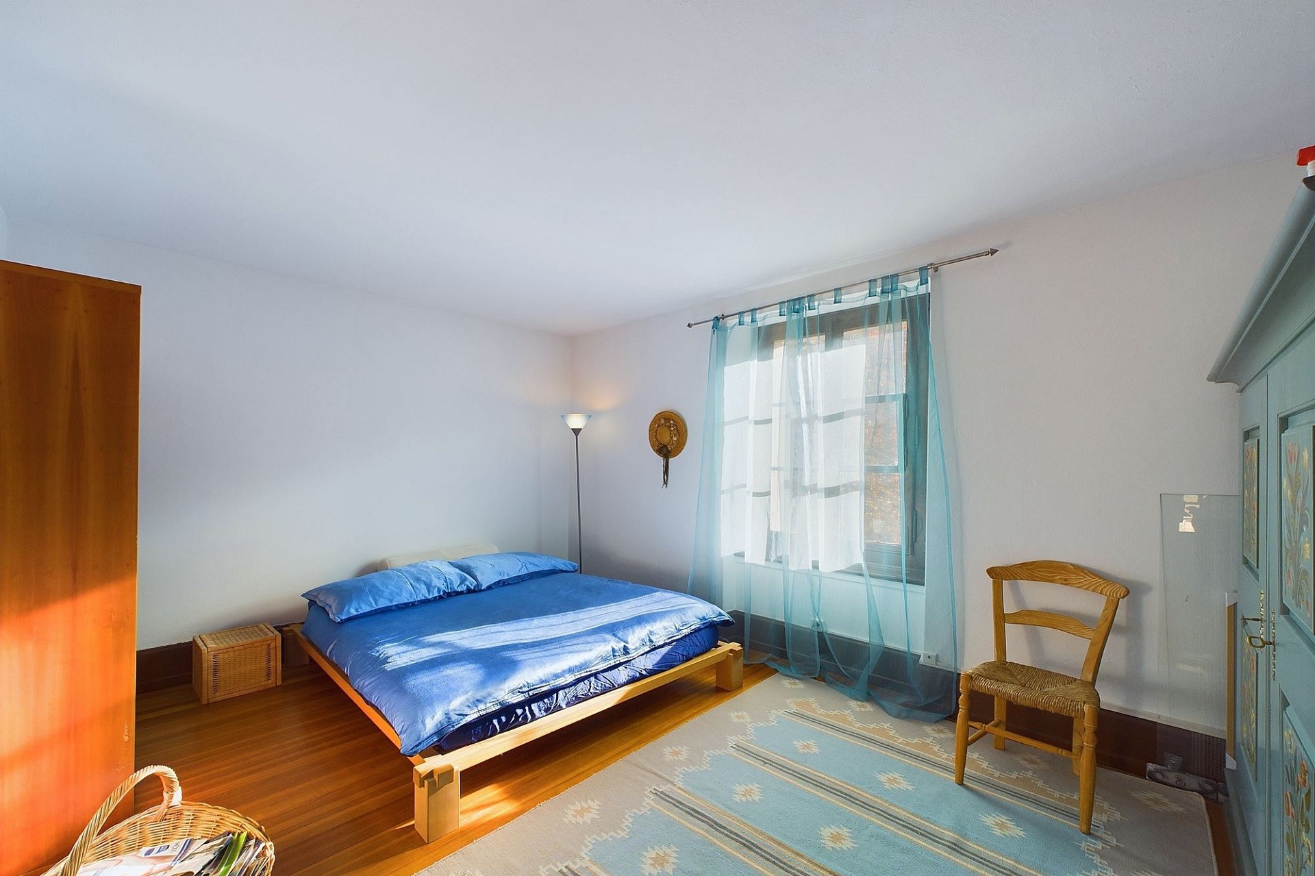 Helles Schlafzimmer mit blauem Bett und Holzmöbeln