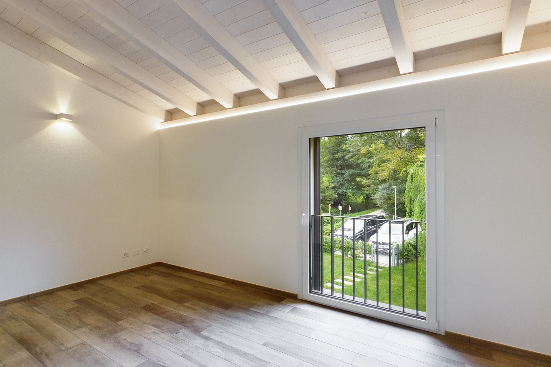 Helles, leeres Zimmer mit Balkontür und Holzbalkendecke