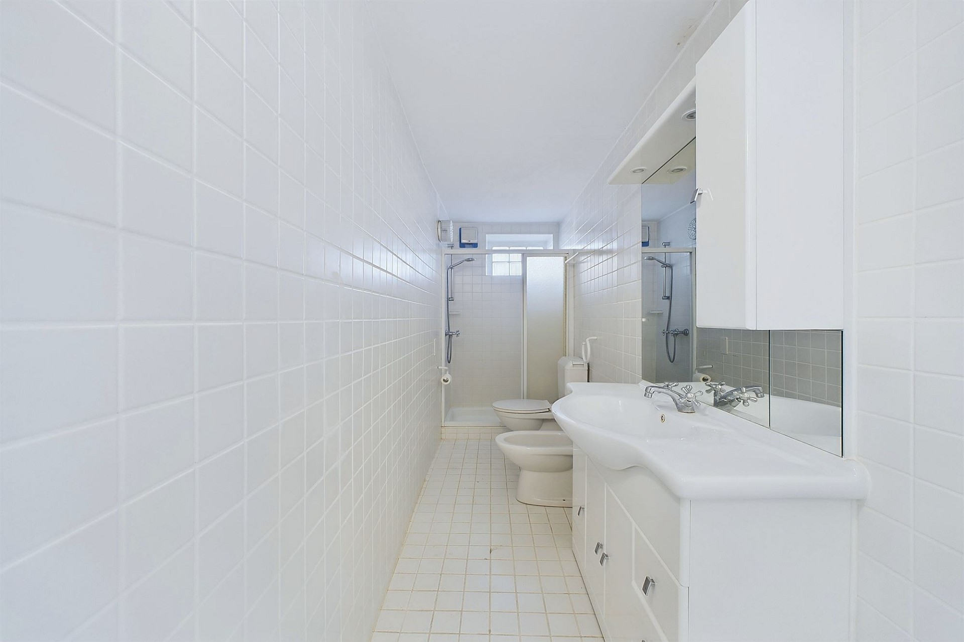 Schmales, weiß gefliestes Badezimmer