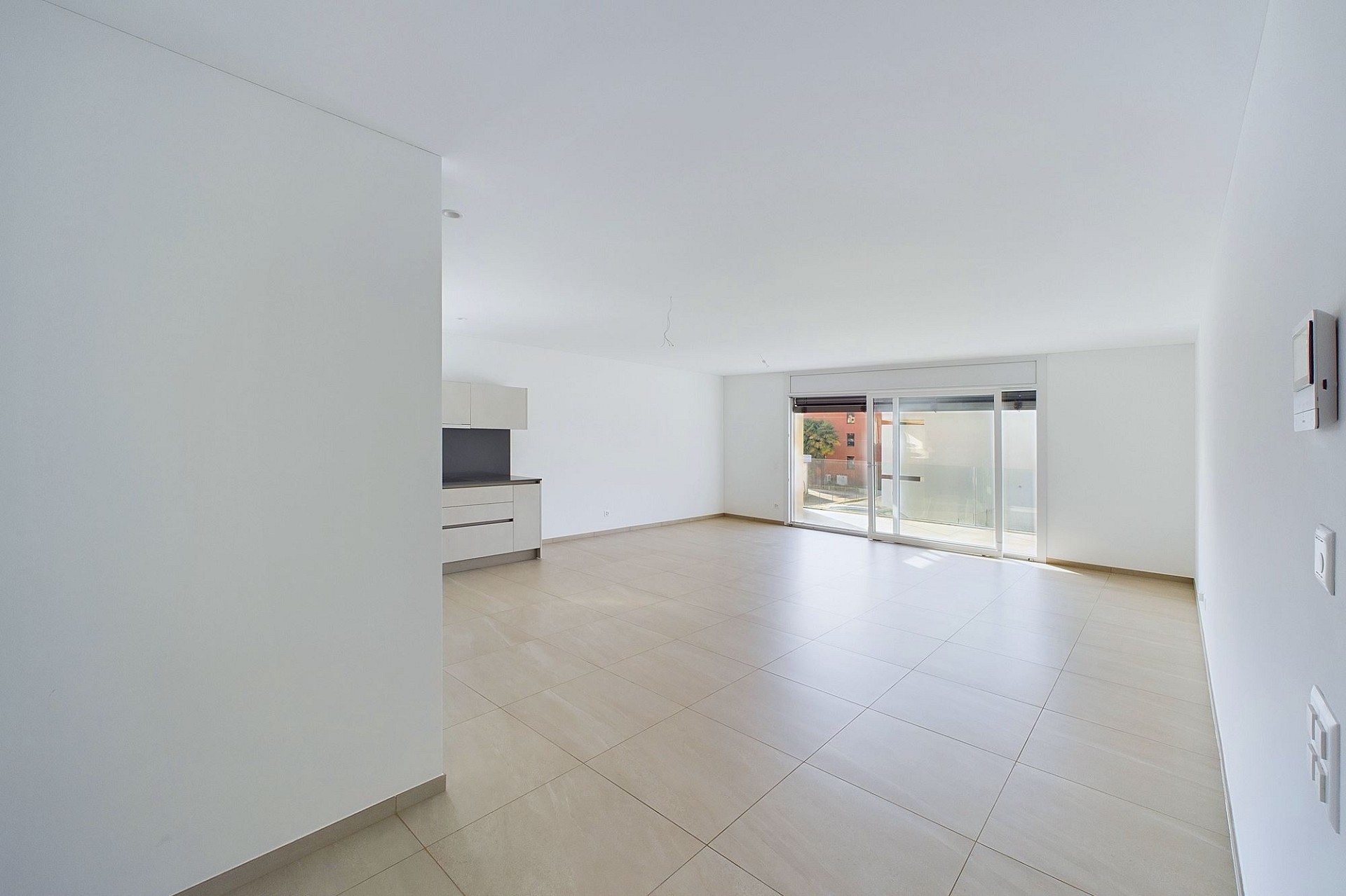 Heller leerer Wohnbereich mit offener Küchenzeile und Balkon-/Terrassentür