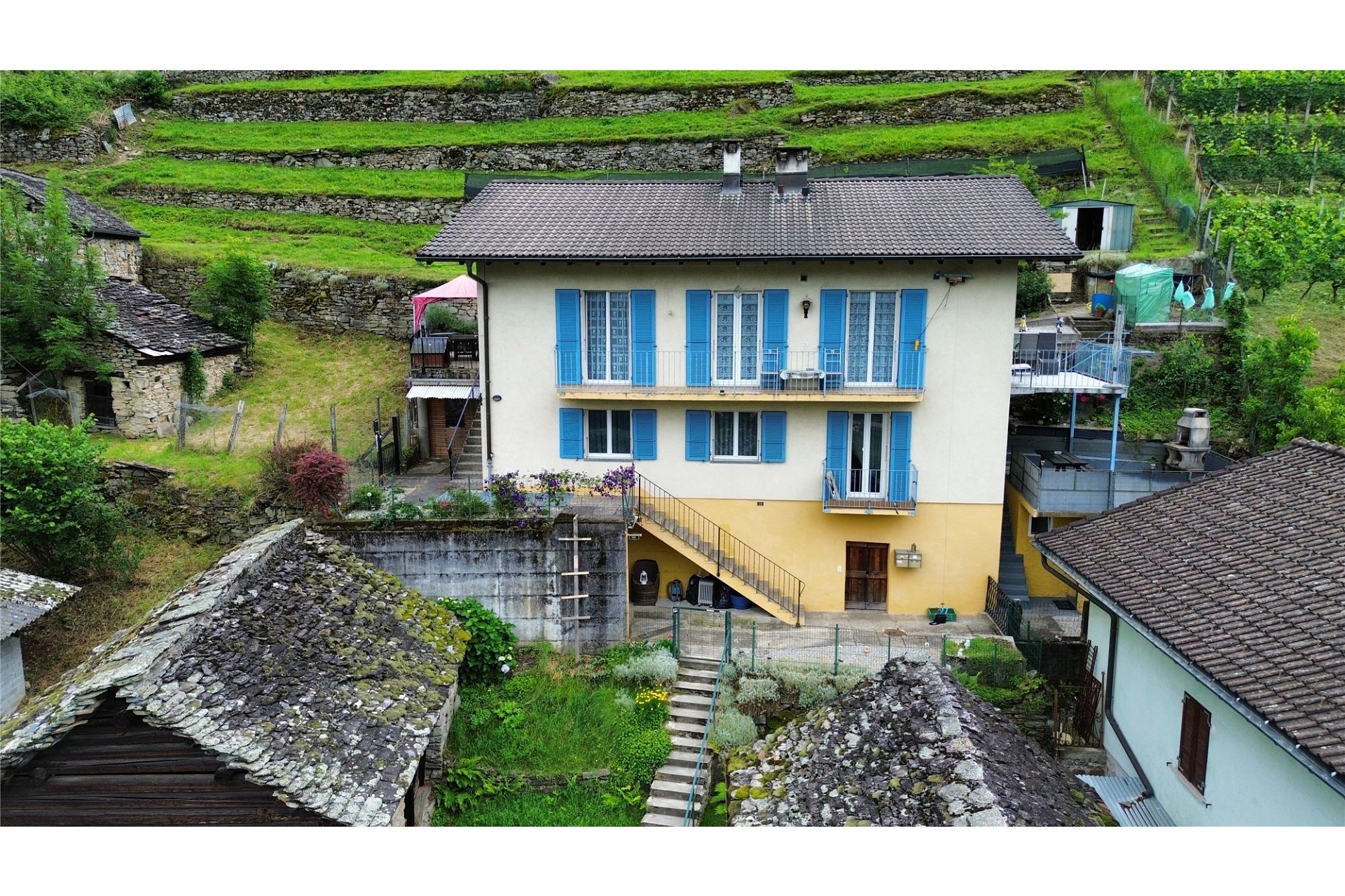 Ländliches Steinhaus mit blauem Fensterladen und terrassiertem Hang