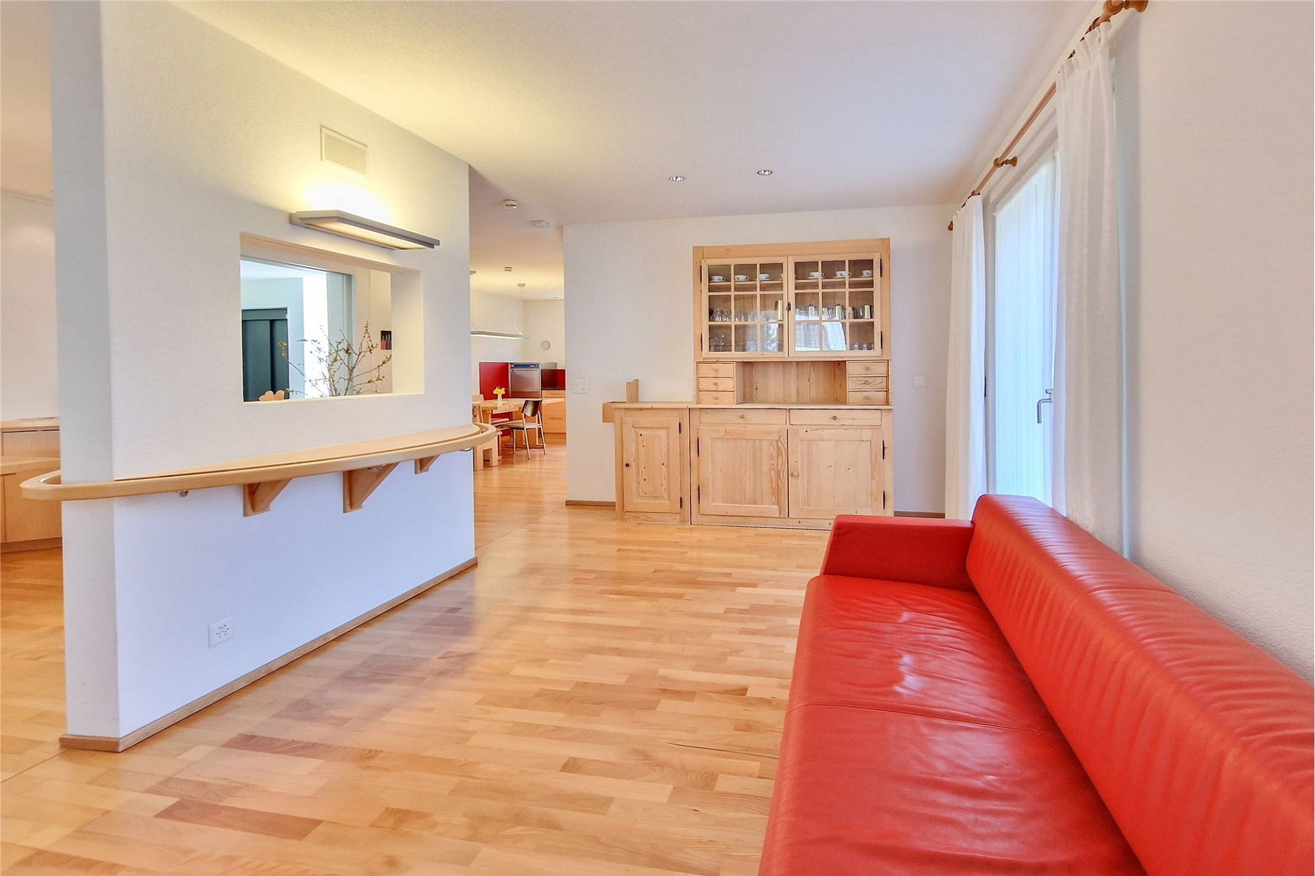Heller Wohnbereich mit rotem Sofa und Holzmöbeln