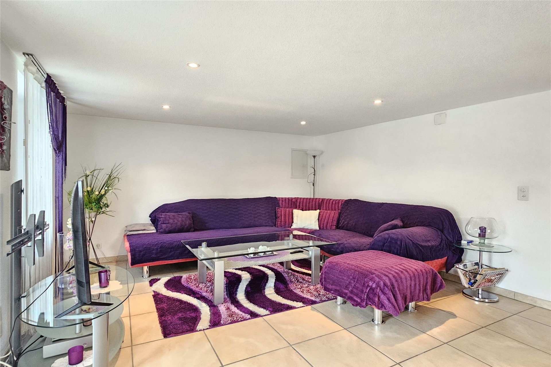 Modernes Wohnzimmer mit L‑Sofa in Violetttönen