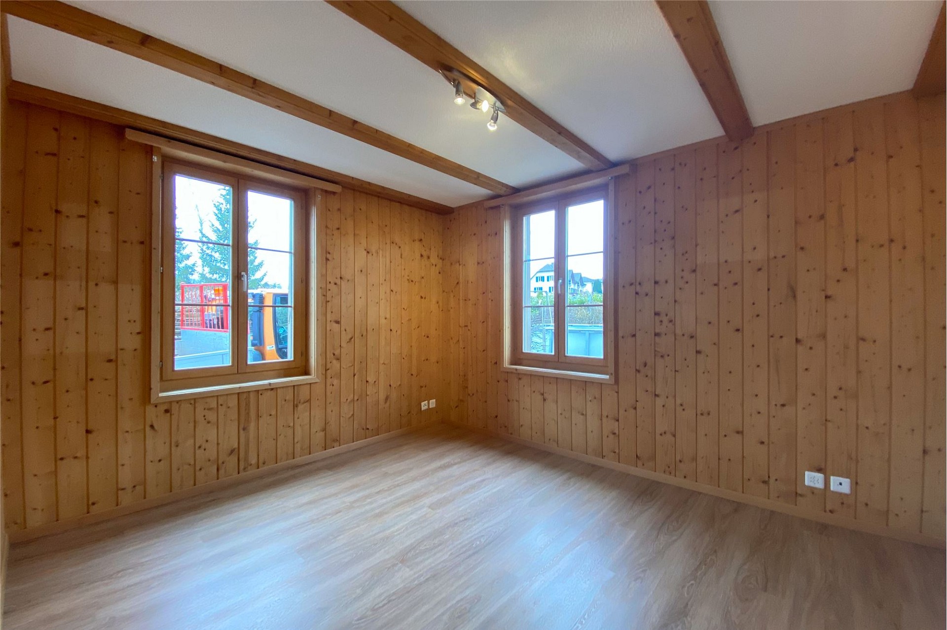 Leerer, holzvertäfelter Raum mit Dachbalken und zwei Fenstern