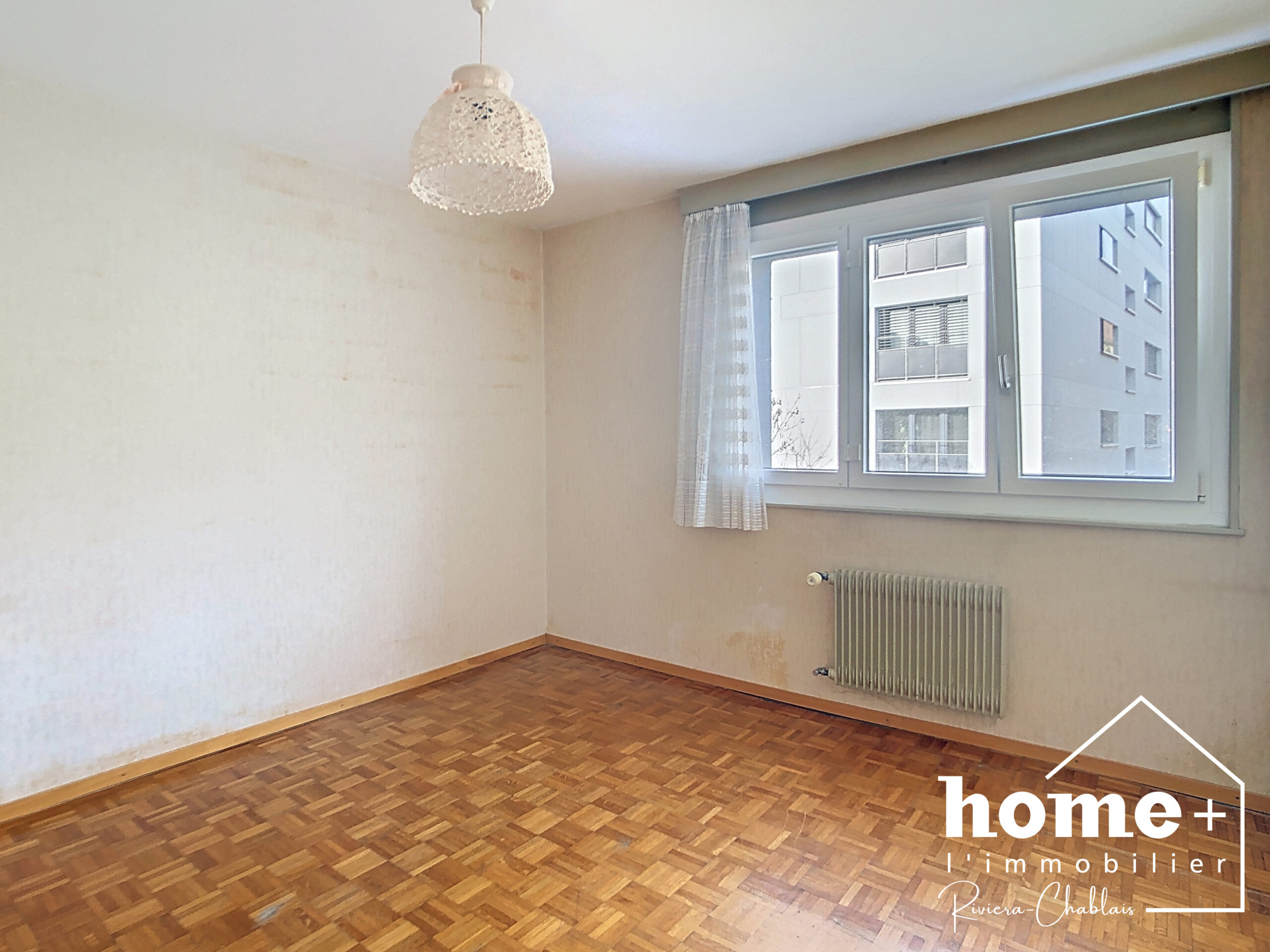 Leerer Wohnraum mit Parkett und großem Fenster