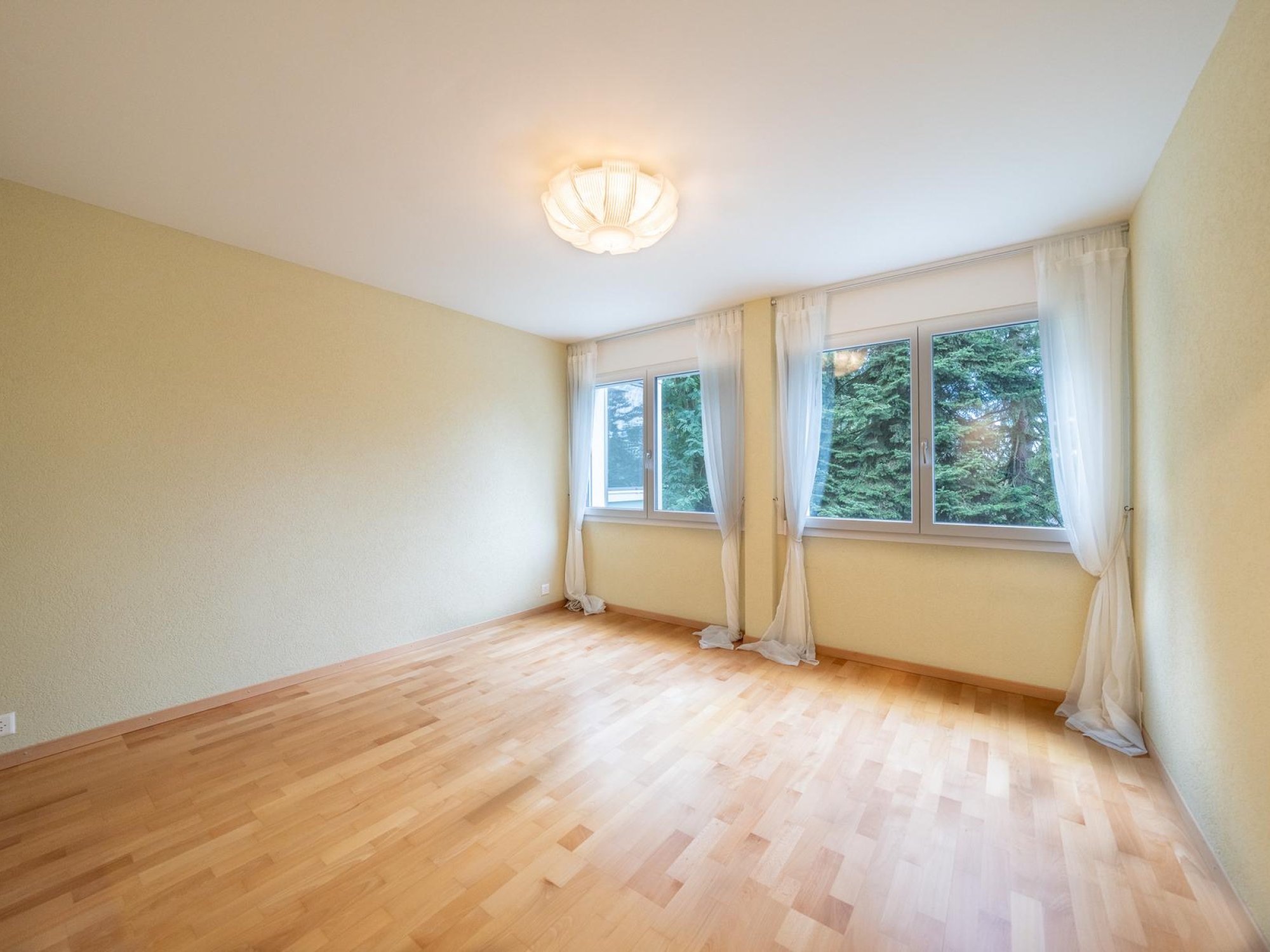 Helles, leeres Schlafzimmer mit Parkett und großen Fenstern
