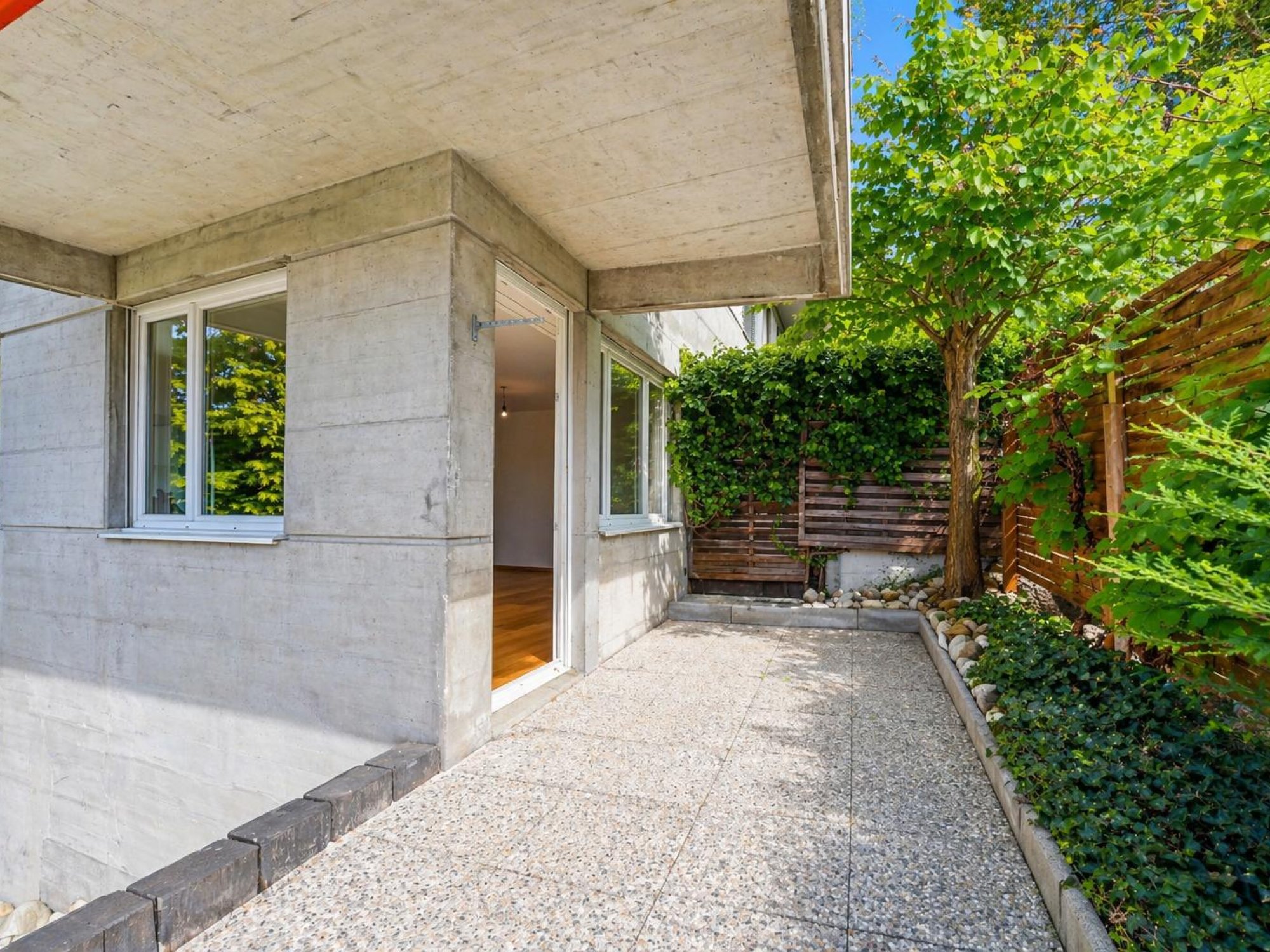 Überdachter Außenbereich mit Betonfassade und begrüntem Patio