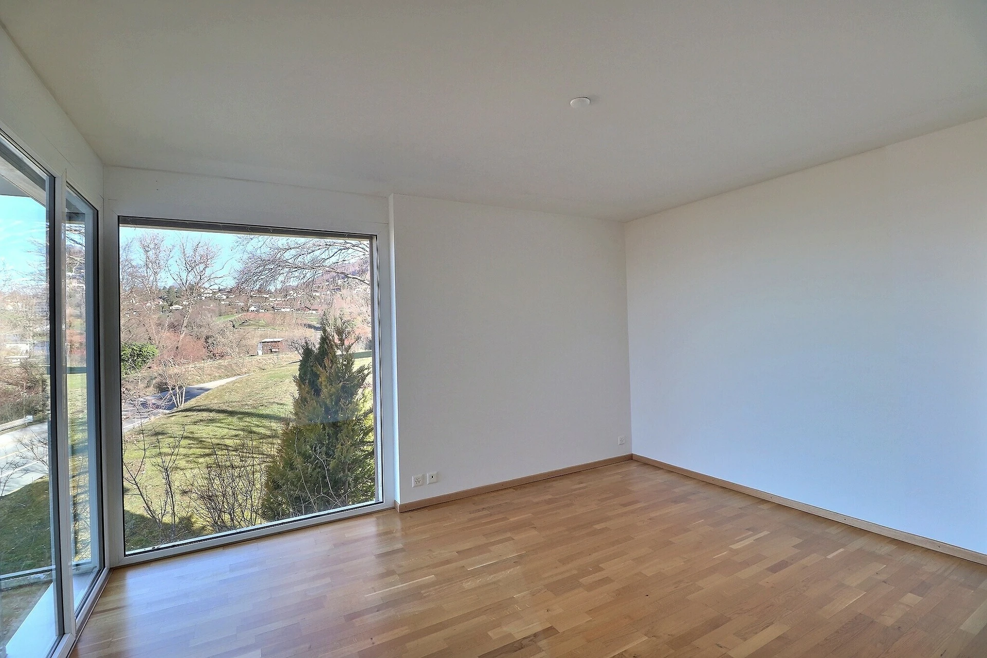 Helles leeres Zimmer mit großem Fenster und Parkettboden