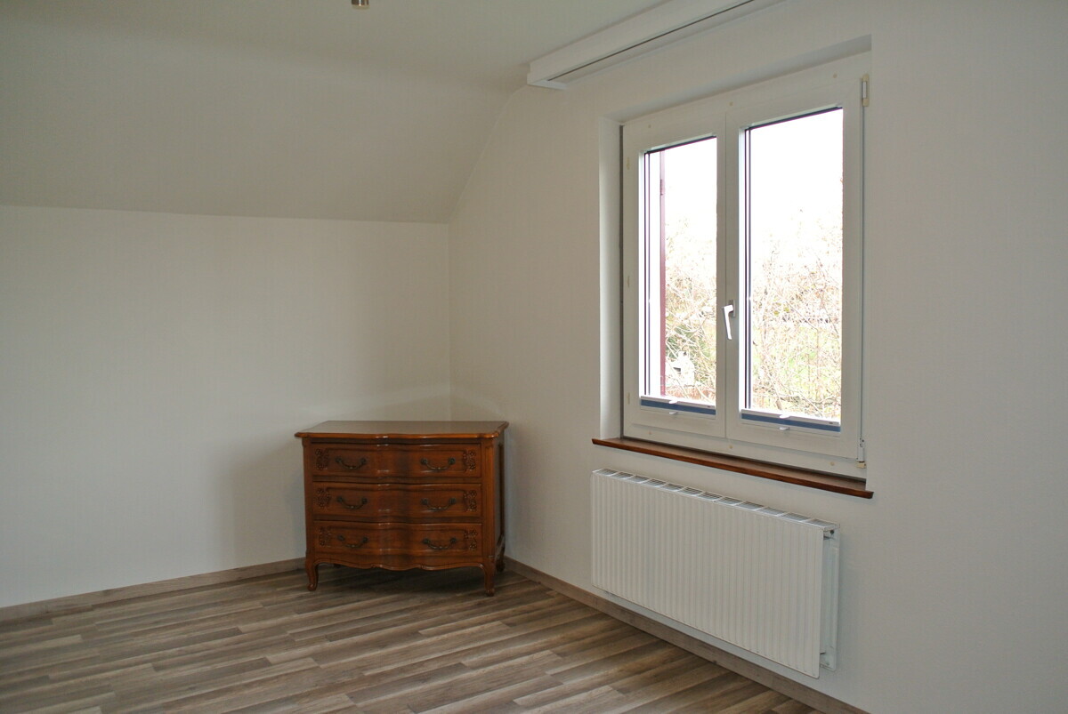Helles, schlichtes Zimmer mit Fenster und antiker Kommode