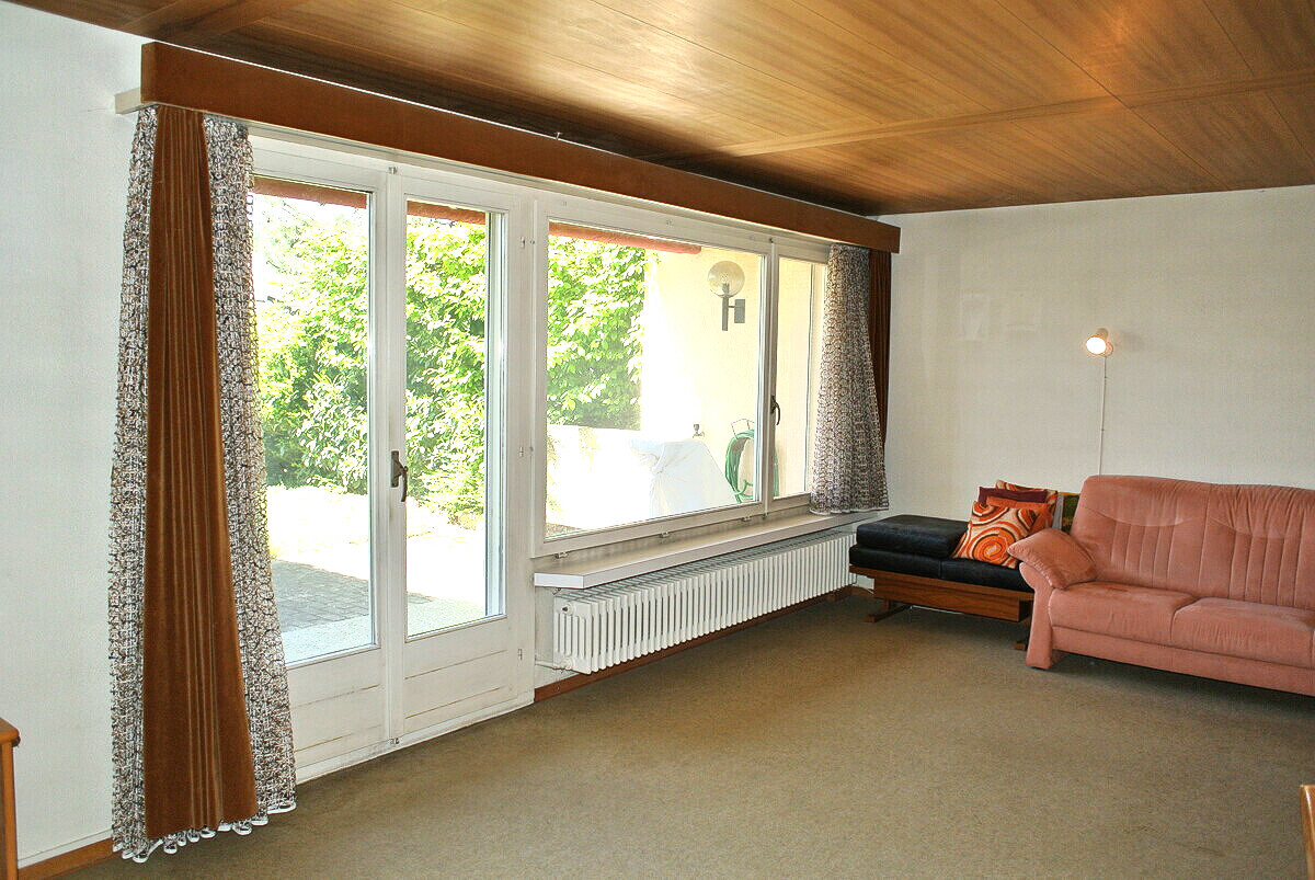 Wohnzimmer mit großer Fensterfront und brauner Holzdecke
