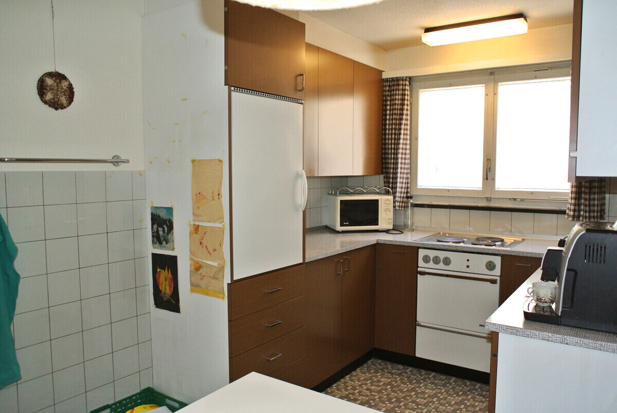Kleine, ältere Küche mit hellen Oberschränken und Fensterarbeitsplatz