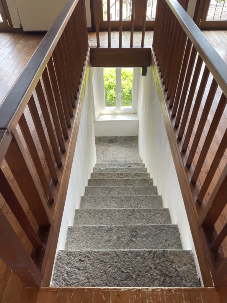 Treppenhaus mit Holzgeländer und Steintreppe
