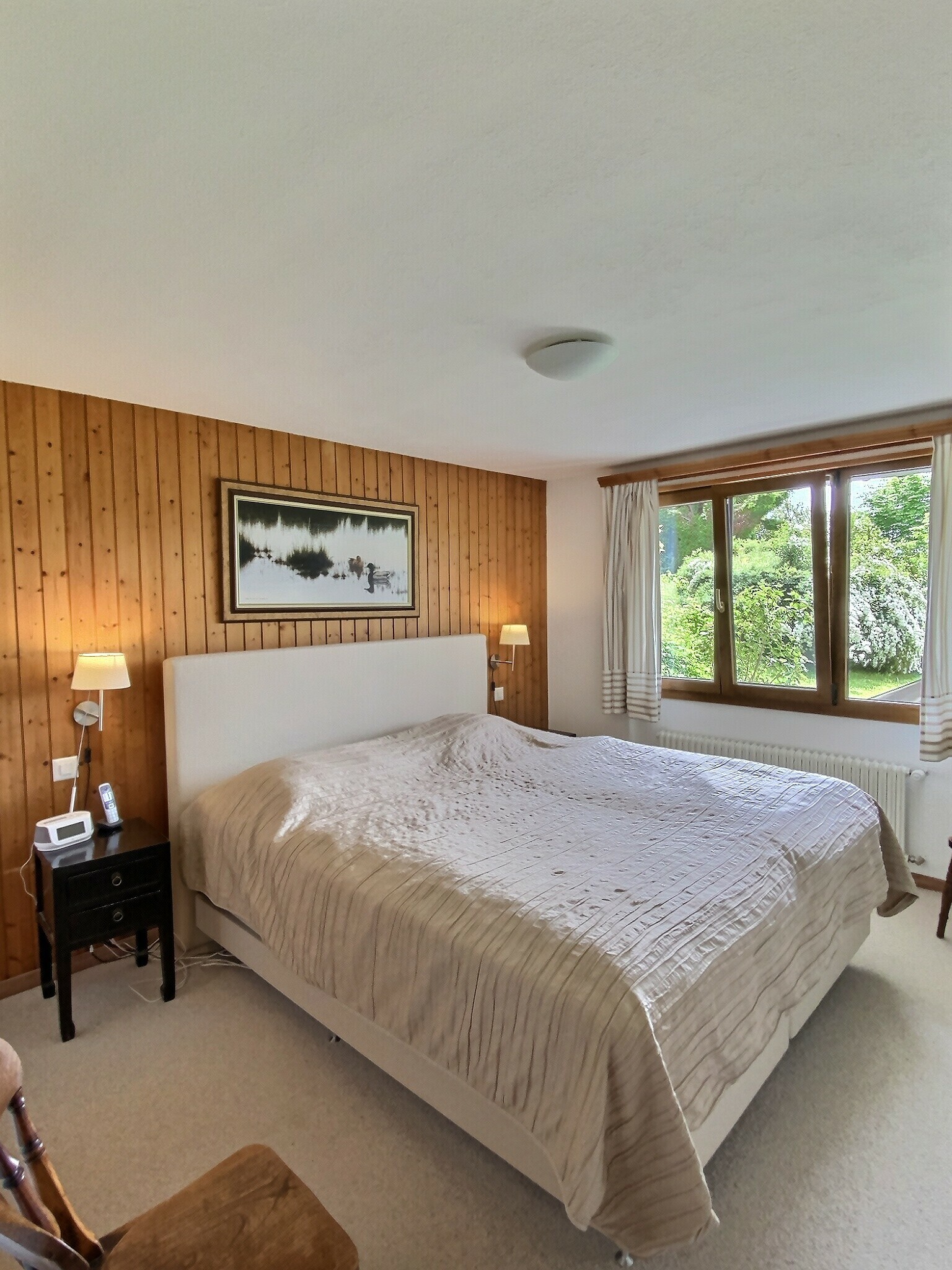 Helles Schlafzimmer mit Holzpaneelwand und Blick ins Grüne
