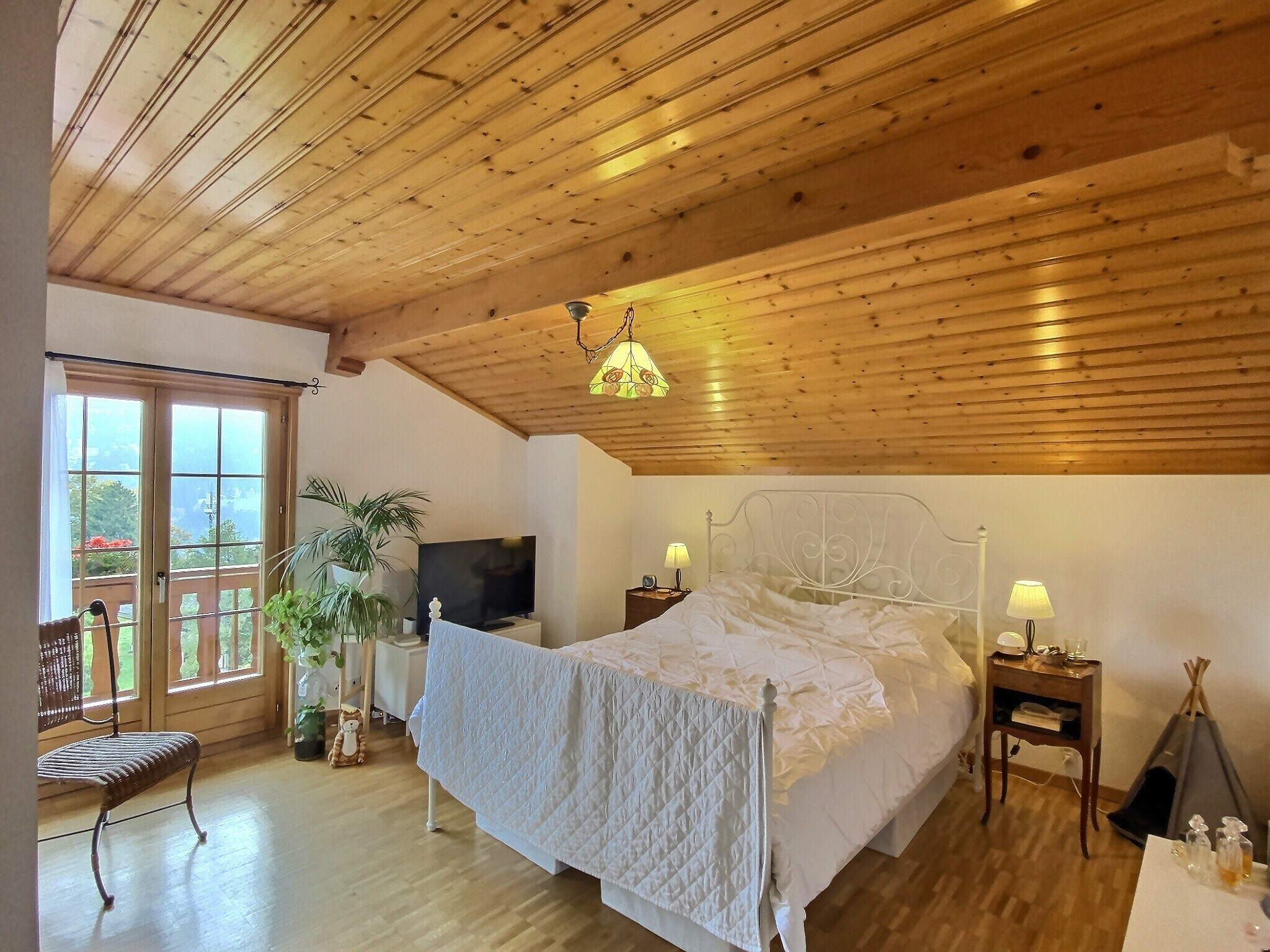 Gemütliches Schlafzimmer mit Holzdecke und Balkonblick