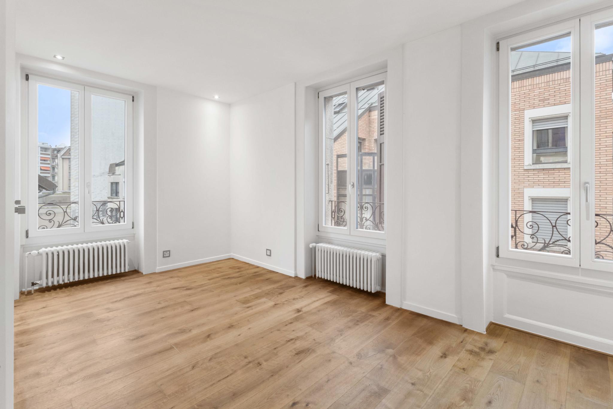 Helles, leeres Zimmer mit drei Fenstern und Holzfußboden