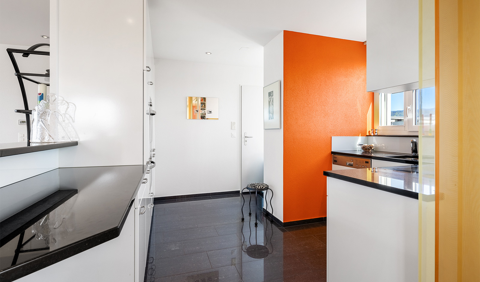 Heller Küchen- und Flurbereich mit auffälliger orangefarbener Wand