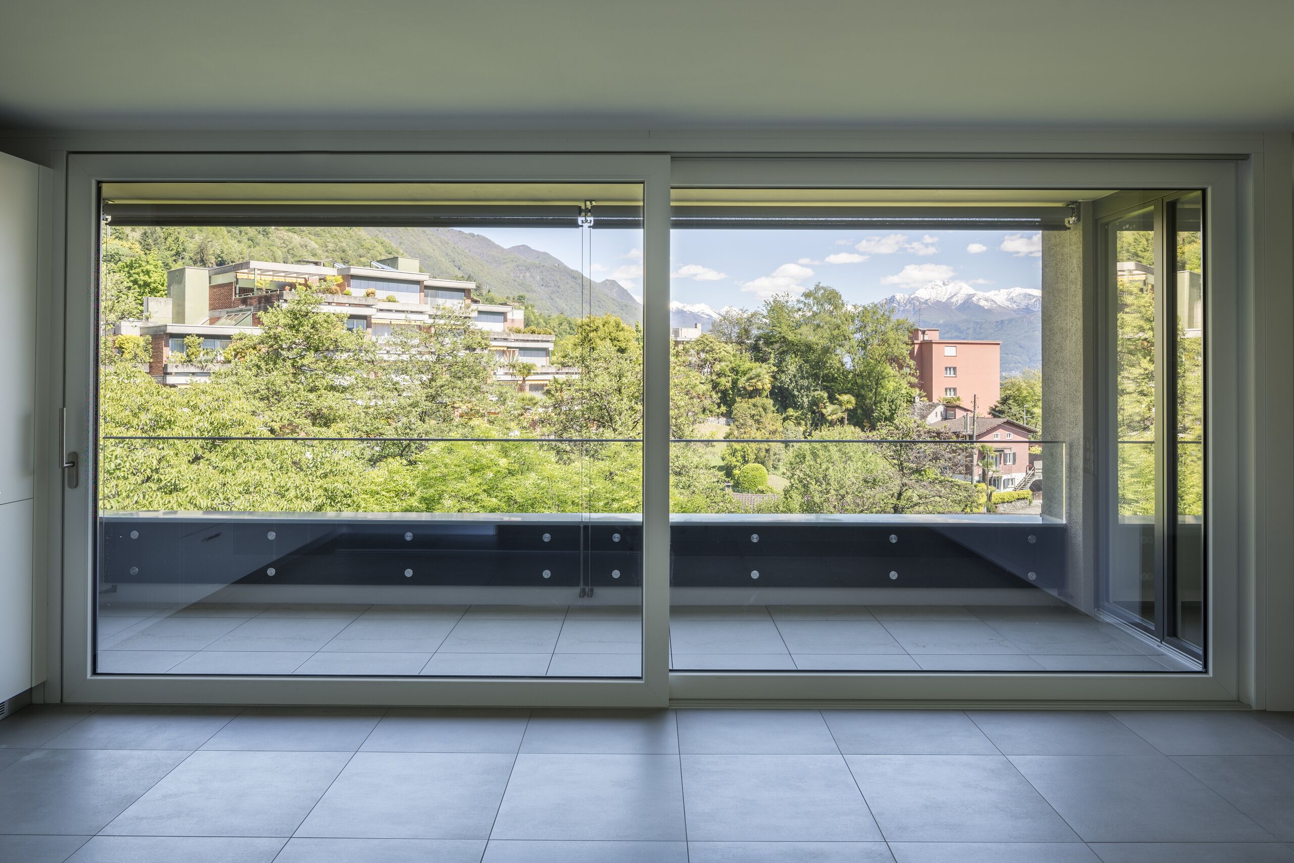 Blick durch bodentiefe Fenster auf Berge und Balkon