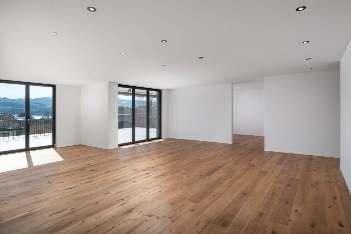 Heller, leerer Wohnbereich mit Holzboden und großen Fenstern