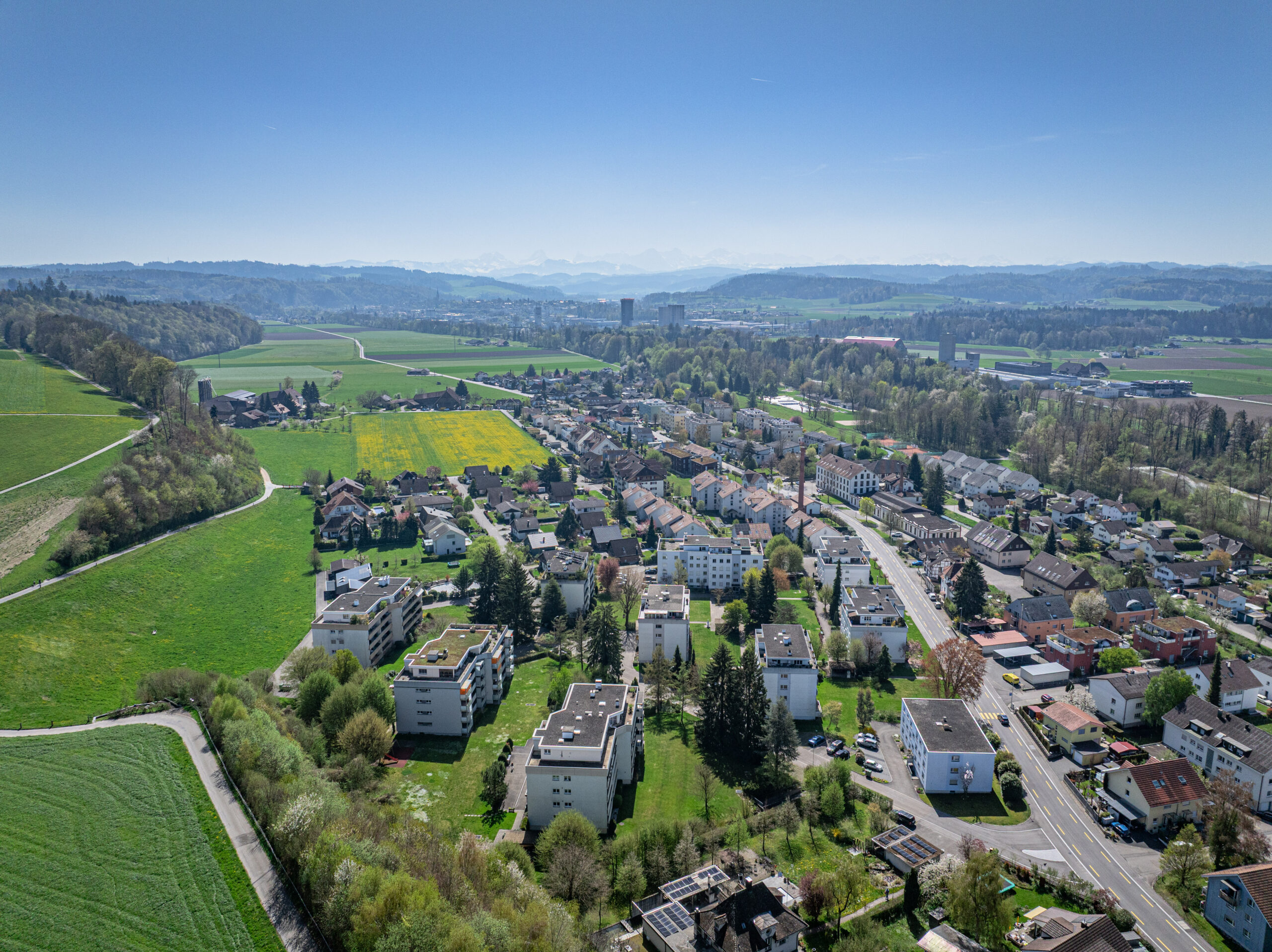 Luftaufnahme einer Wohnsiedlung in grüner Landschaft mit Bergblick