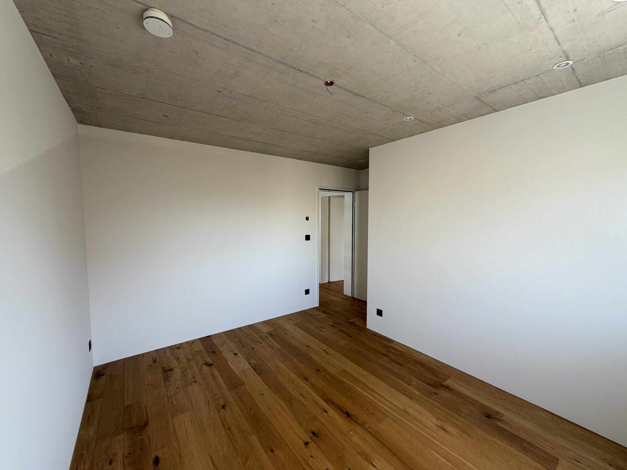 Leerer, modern gestalteter Raum mit Holzfußboden und Sichtbetondecke