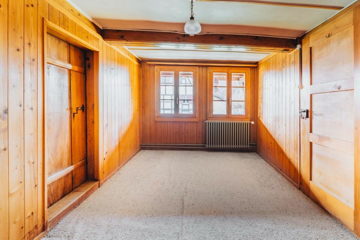 Heller holzvertäfelter Raum mit zwei Fenstern und Heizkörper