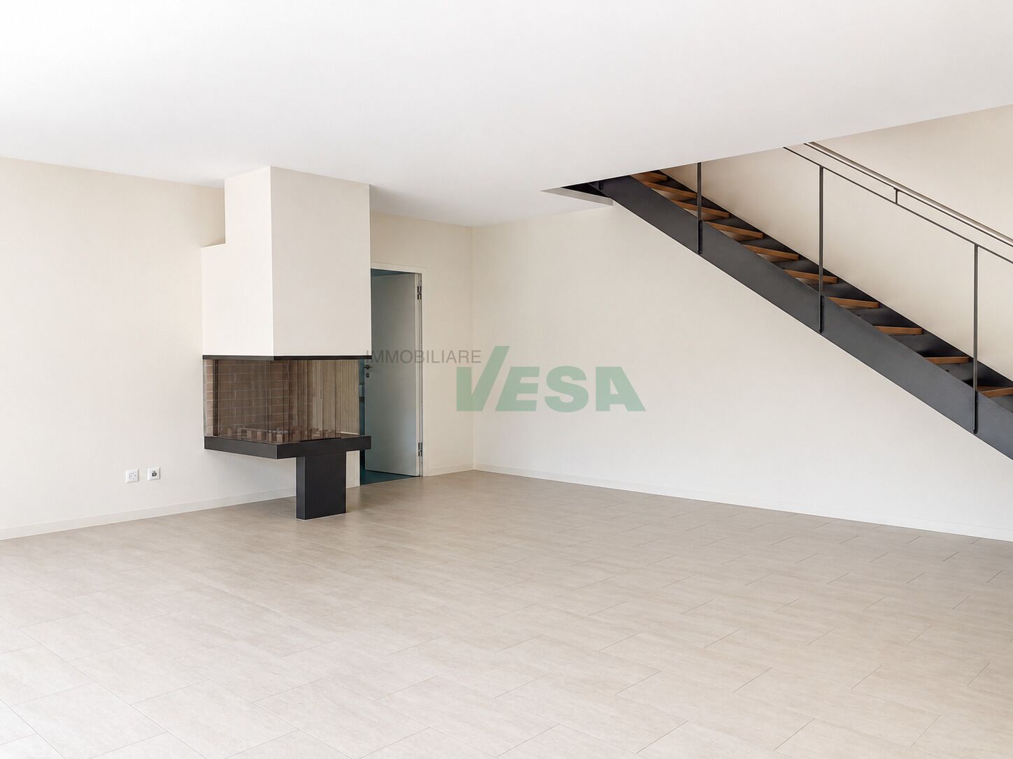 Großer leerer Wohnraum mit Treppe und Kamin
