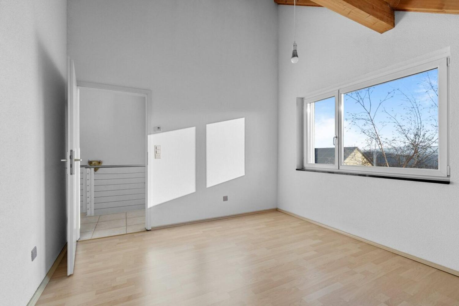 Helles, leeres Zimmer mit Holzdecke und großem Fenster