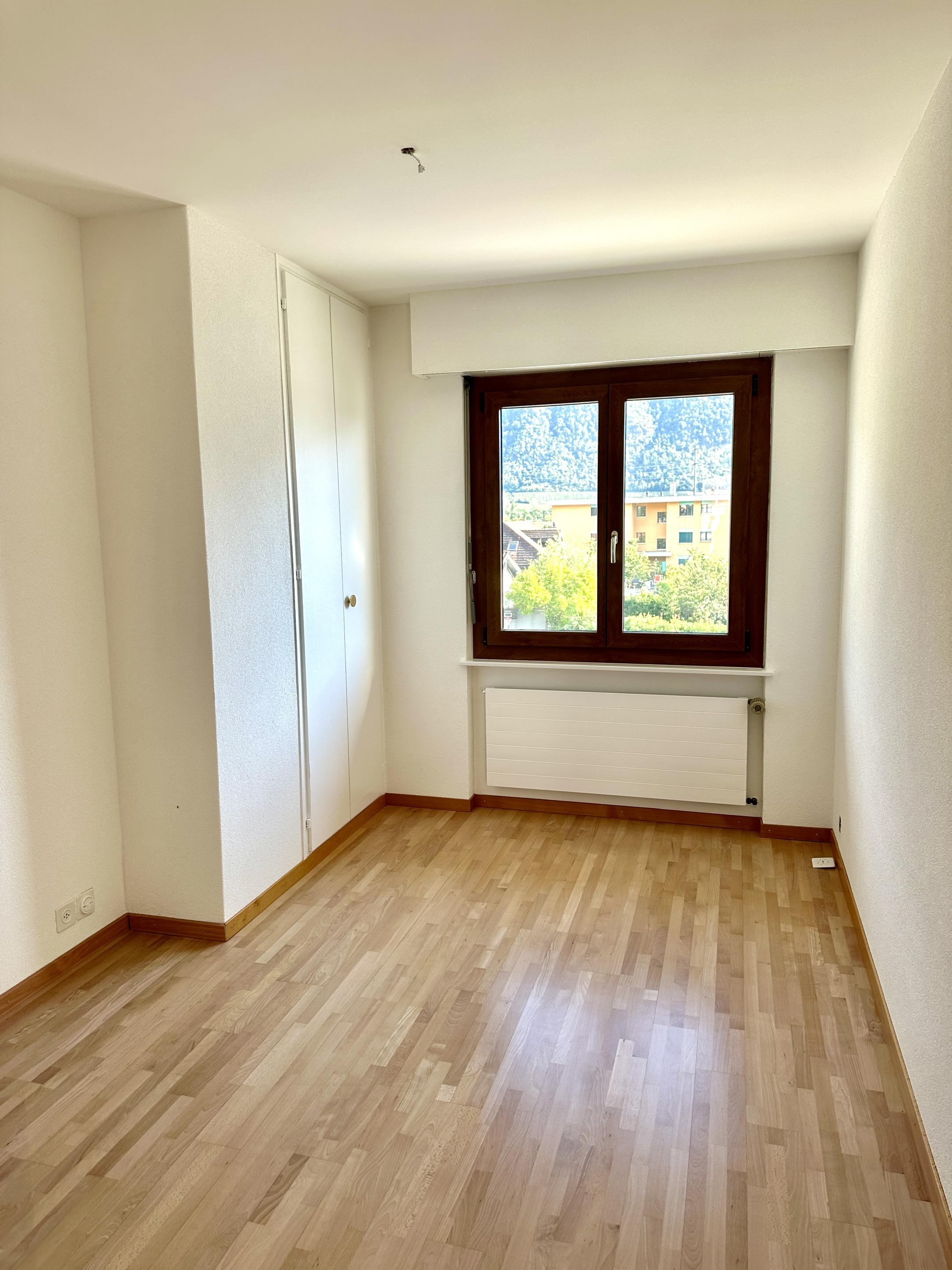 Helles, leeres Zimmer mit Holzfußboden und Fenster