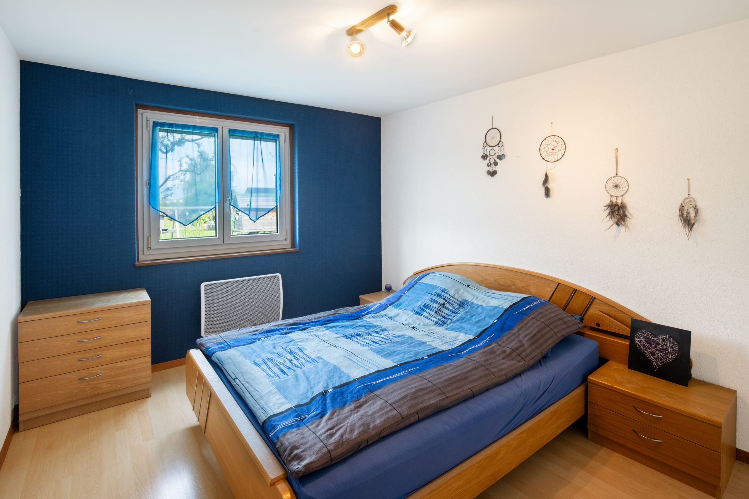 Schlafzimmer mit blau akzentuierter Wand und Holzmöbeln