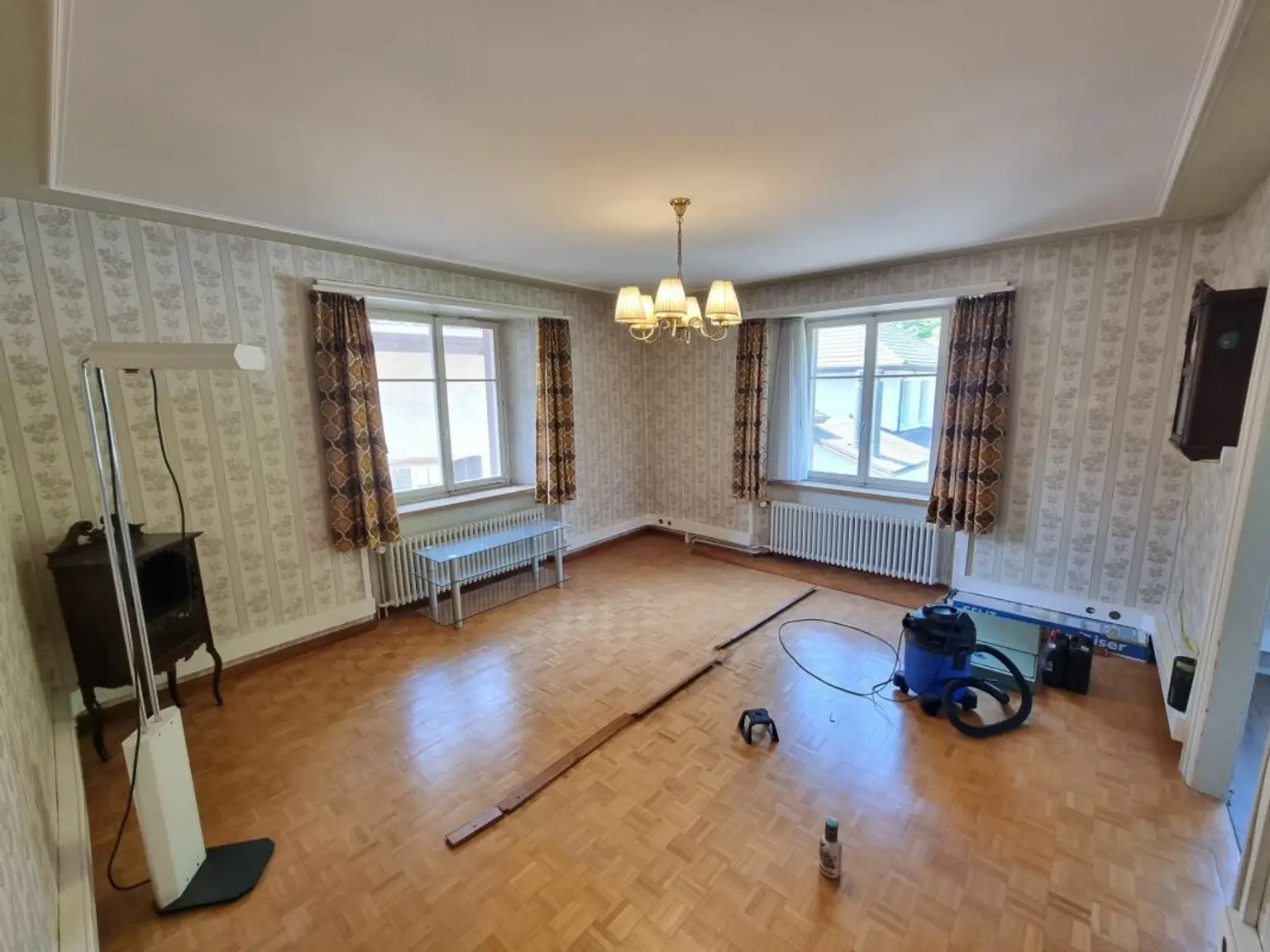 Altmodisches Wohnzimmer mit Tapeten, zwei Fenstern und Parkettboden