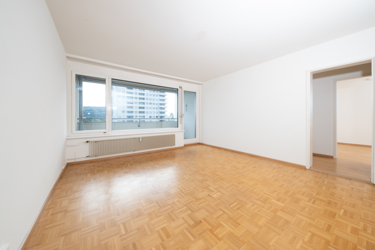 Heller leerer Wohnraum mit Parkettboden und großem Fenster