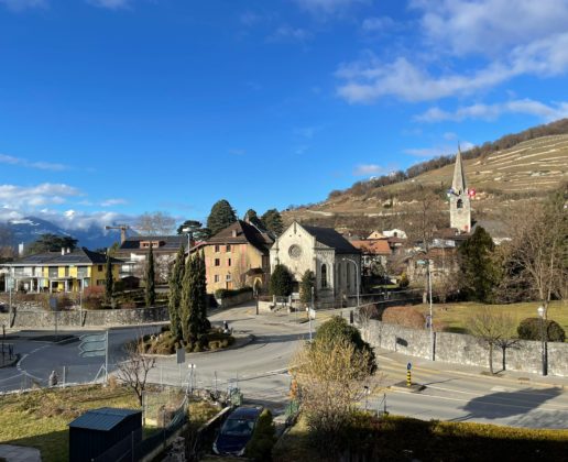 Dorfansicht mit Kirche und Hügeln