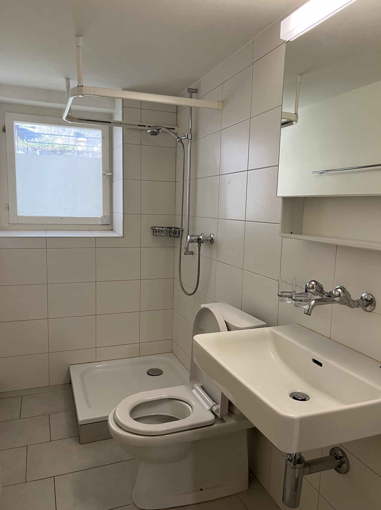 Kleines weiß gefliestes Badezimmer mit Dusche, WC und Waschtisch