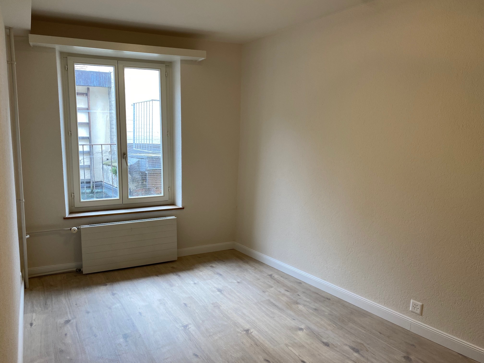 Leerer, heller Raum mit Fenster und Heizkörper