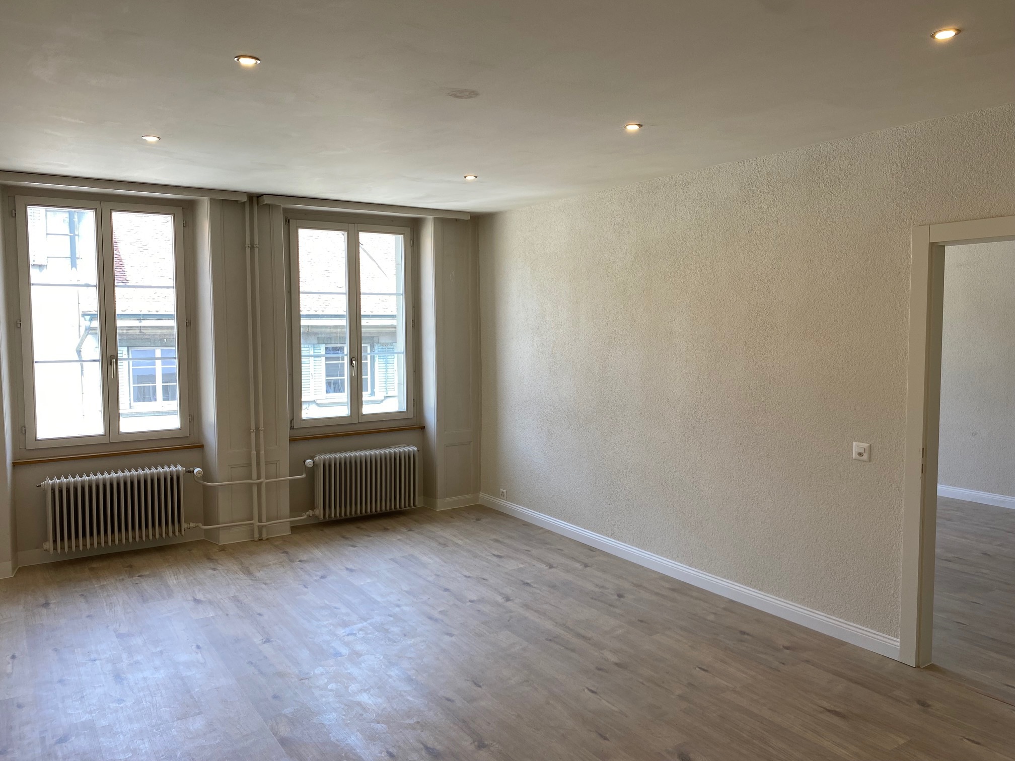 Helles, leeres Wohn-/Schlafzimmer mit zwei Fenstern und Heizkörpern