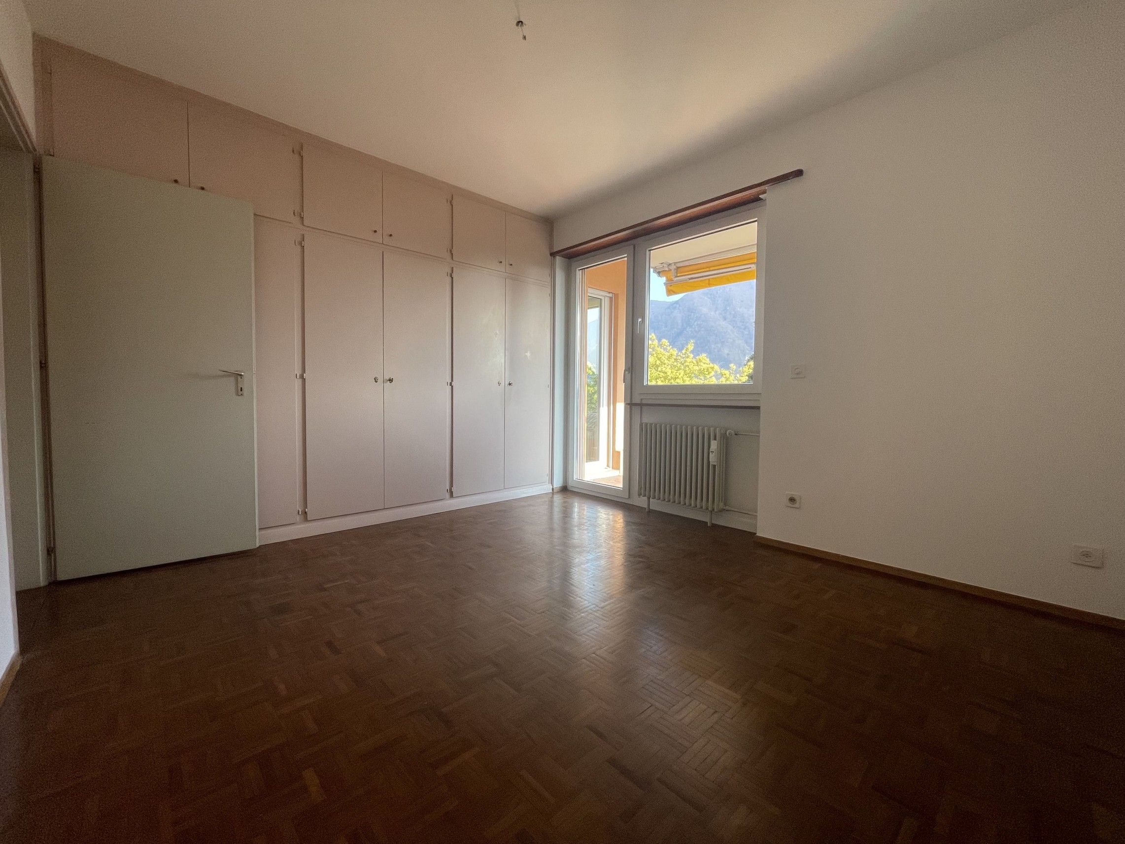 Leerer Wohnraum mit Einbauschränken und Balkonblick