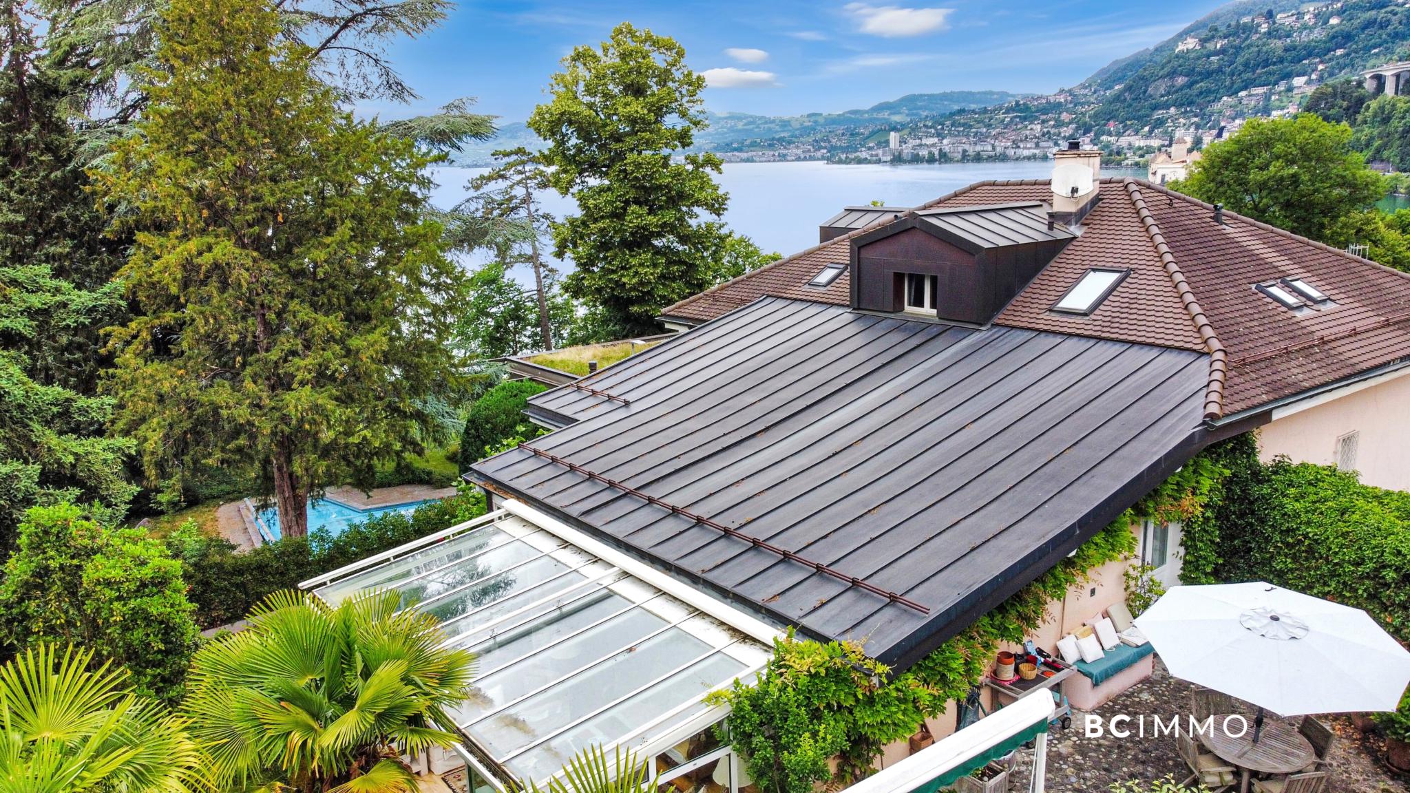 Seeblick auf ein Haus mit großer Dachlandschaft und Garten