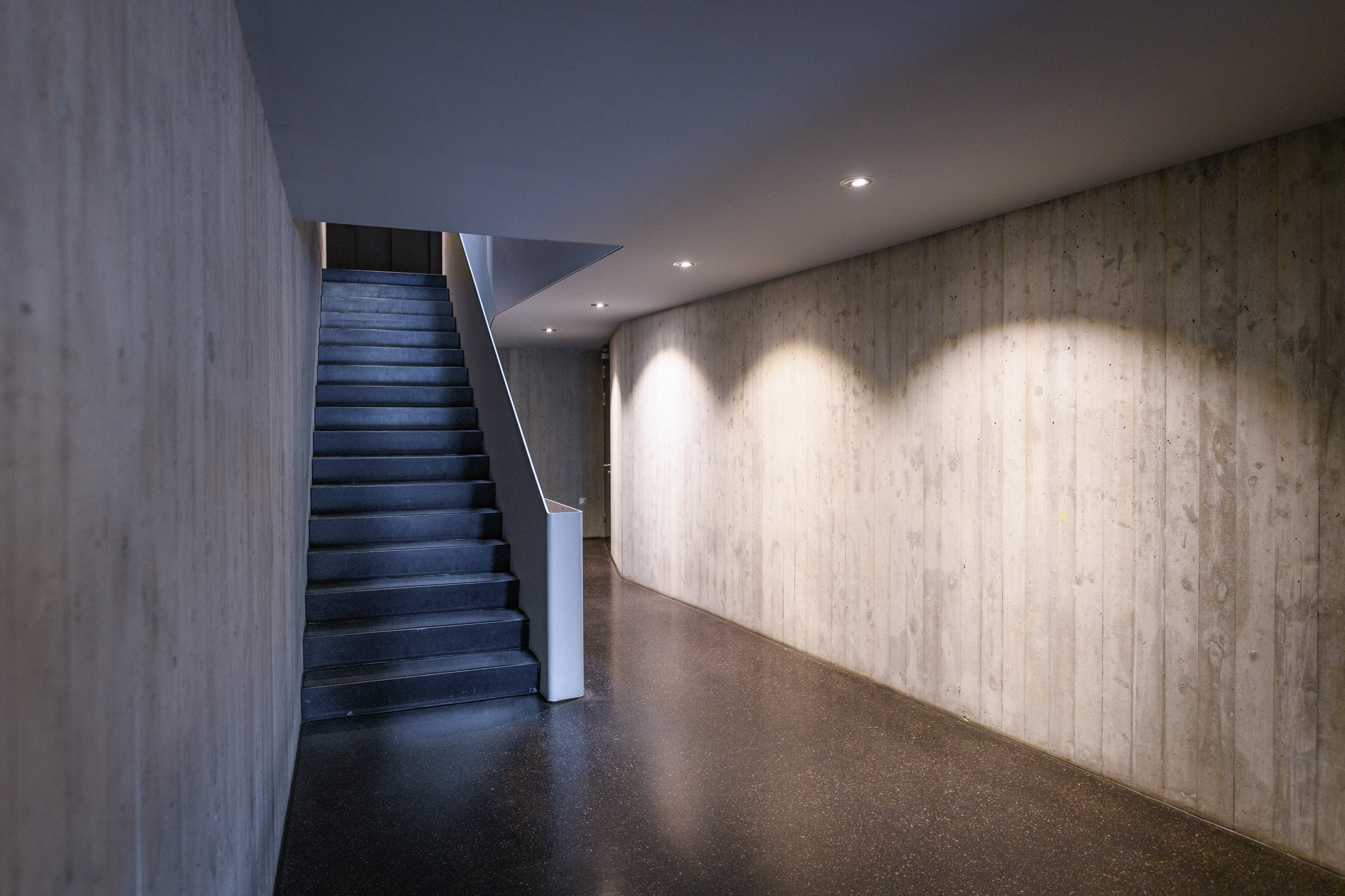 Moderner Treppenflur mit Sichtbeton und dunklem Boden